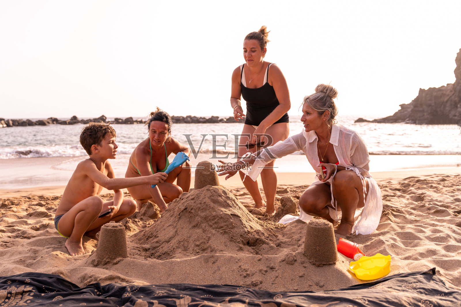 度假的一家人在日落时分的海滩上玩沙堡照片摄影图片