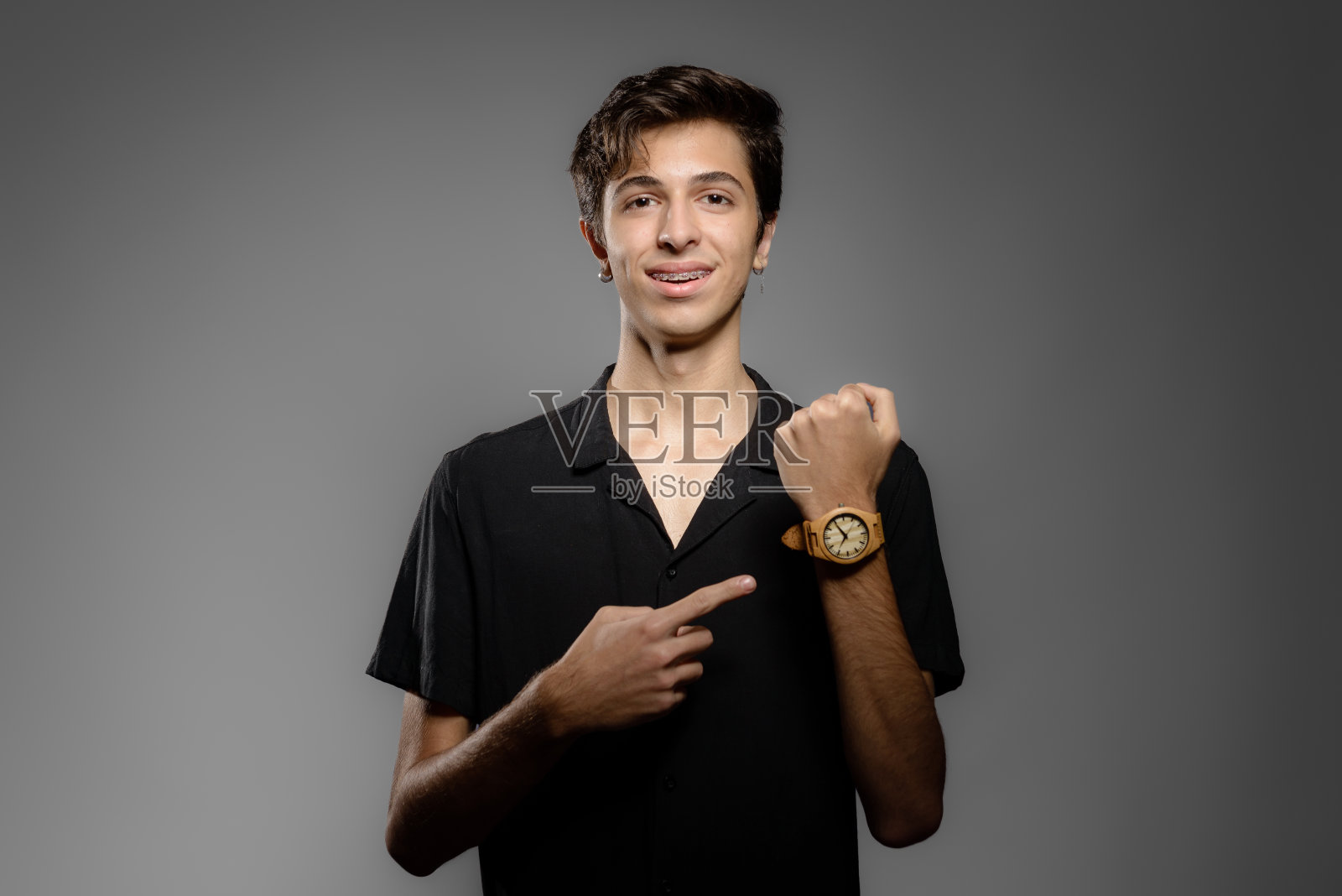 画像的年轻人看着相机，指着手表照片摄影图片