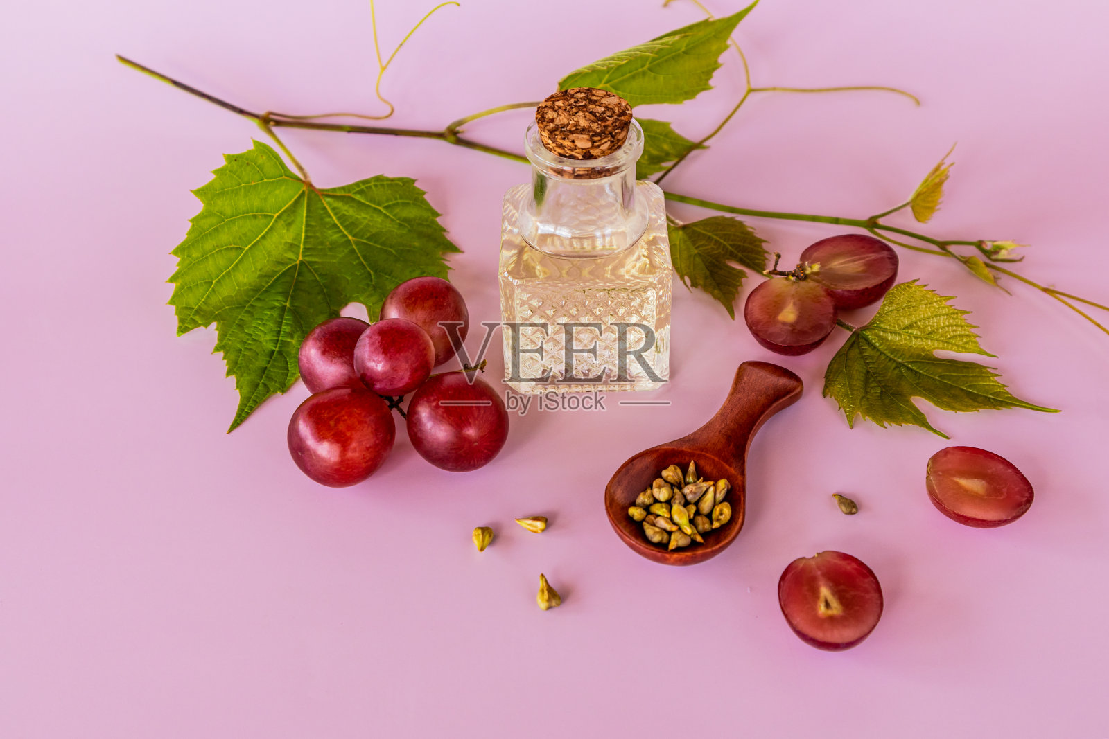 葡萄籽油在一个透明的玻璃瓶与塞子在一个粉红色的背景和藤蔓。维生素、矿物质含量高。照片摄影图片