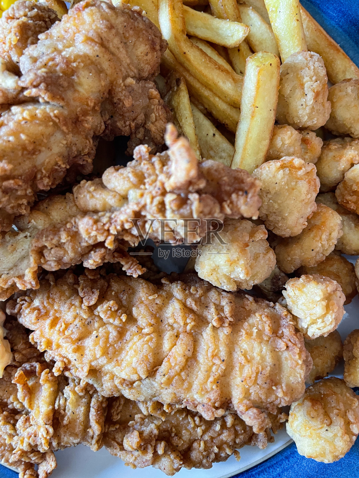 全帧图像蓝色边框的盘子包含南方炸鸡片，爆米花鸡片和薯条，捶打鸡胸片和炸薯条，高架视图照片摄影图片