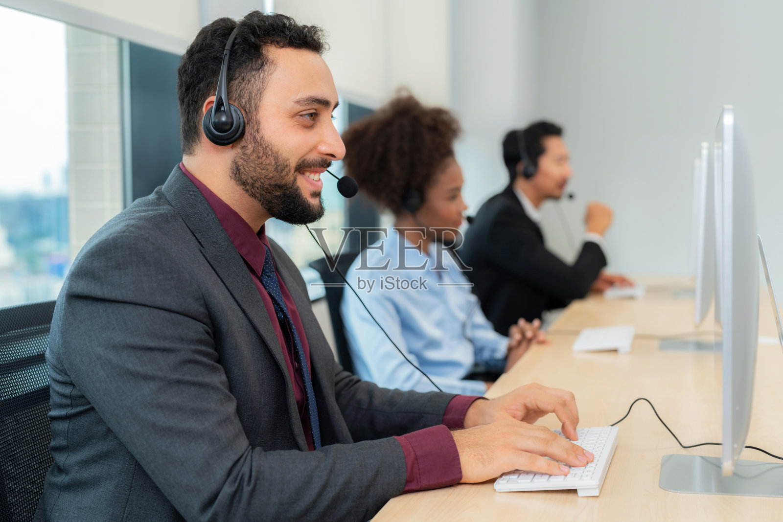一位在呼叫中心工作的资深、自信、友好的话务员，配有耳机和电脑
现代办公室。用微笑解决客户的问题。客户支持和团队合作理念照片摄影图片