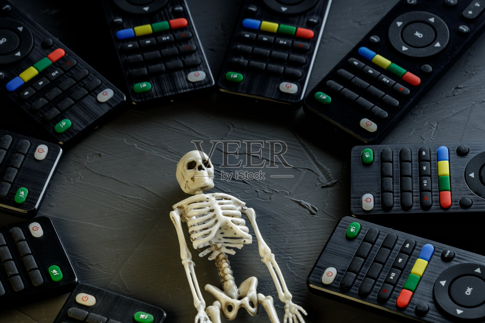 在黑暗的表面上有一个男人的骨架，周围有电视的遥控器照片摄影图片