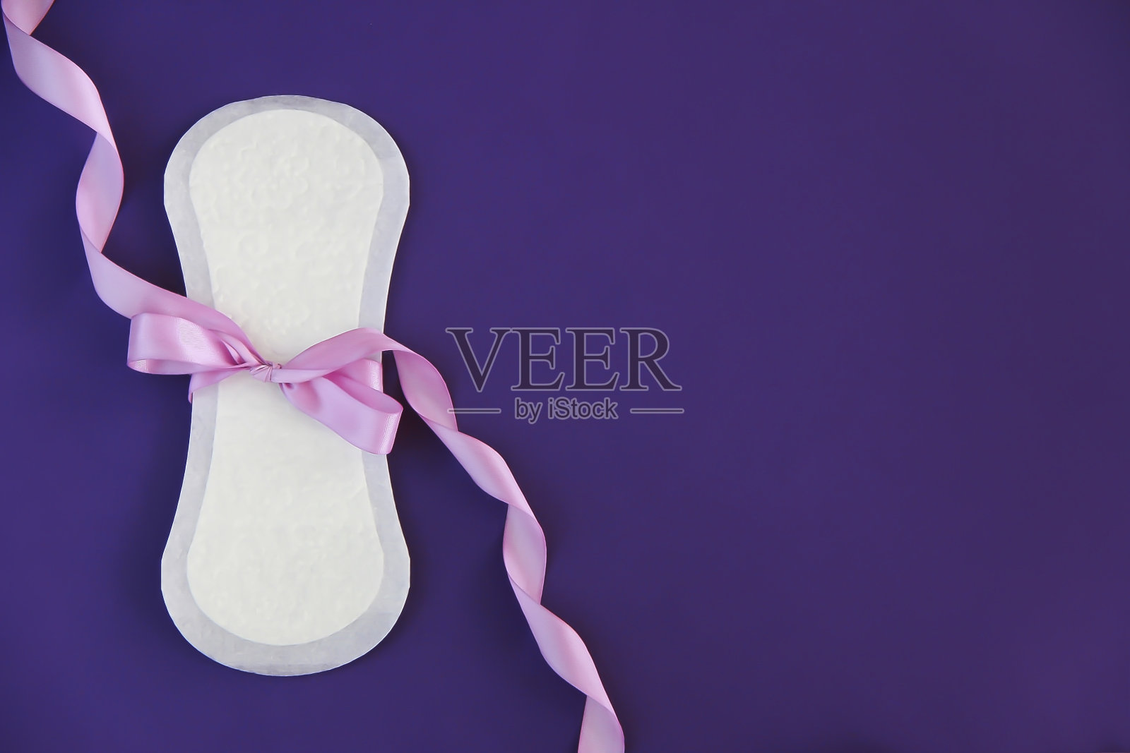 白色卫生女性生理分泌物垫，装饰有粉红色的蝴蝶结，在紫色的背景照片摄影图片