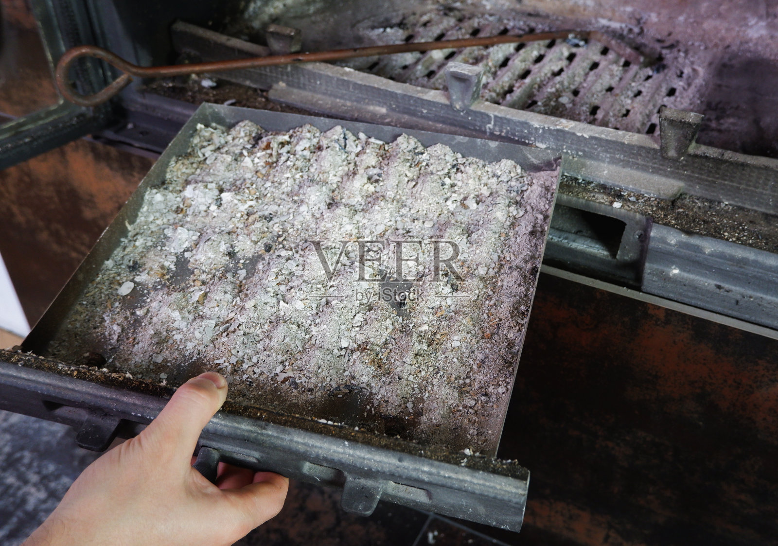 壁炉的清洁。男人手里拿着一把带灰的铲子。一只手在一把旧钢刃上收集壁炉里的灰。冬天每天例行的照片摄影图片