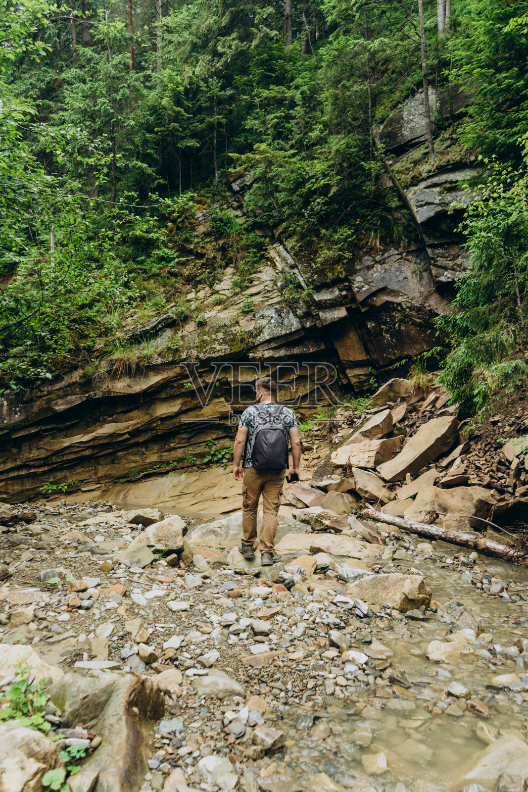 盖伊游客以山石和针叶树为背景。一个背着旅游背包的年轻人穿过山间河流的岩石。照片摄影图片