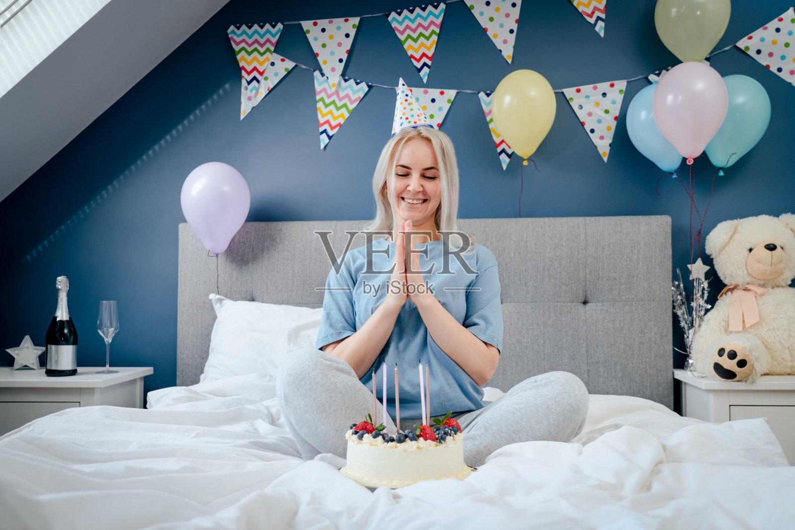 在吹灭生日蛋糕上的蜡烛后，快乐的情绪化的女人坐在装饰好的卧室的床上。许愿的过程。早上意外。生日快乐的概念。照片摄影图片