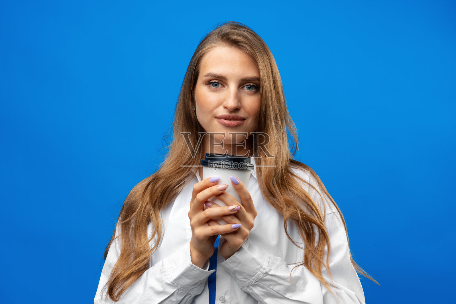美丽迷人的年轻女士拿着外卖纸咖啡杯在蓝色背景的工作室照片摄影图片