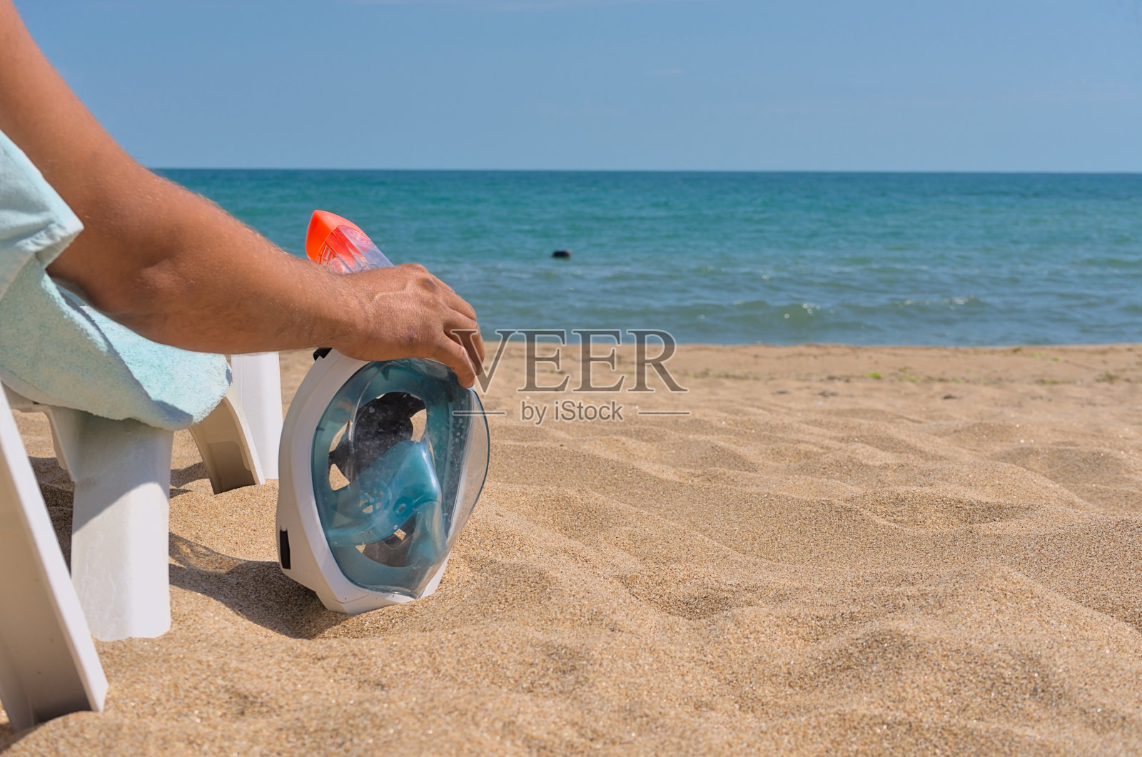男子躺在沙滩上白色的日光躺椅上，手持潜水面罩照片摄影图片