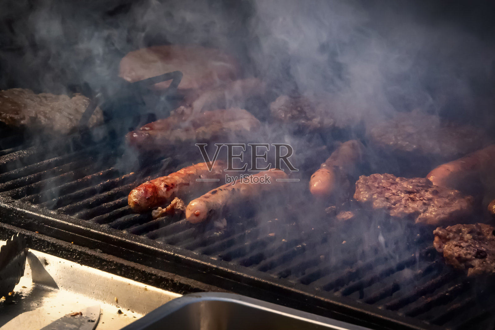 香肠和汉堡肉片在烤架上冒着烟炸照片摄影图片