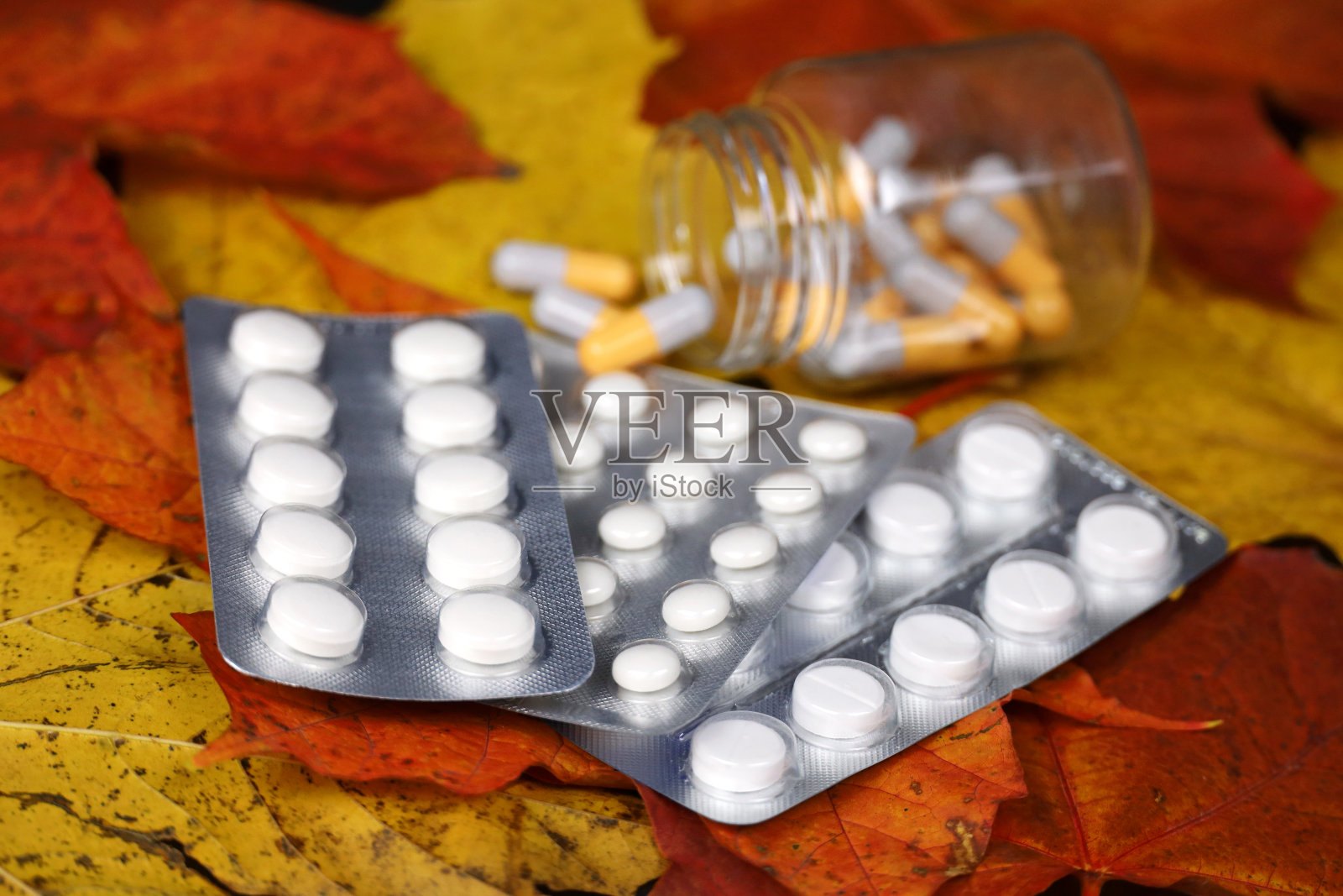黄色和红色枫叶上的药丸、胶囊瓶和药片包装照片摄影图片