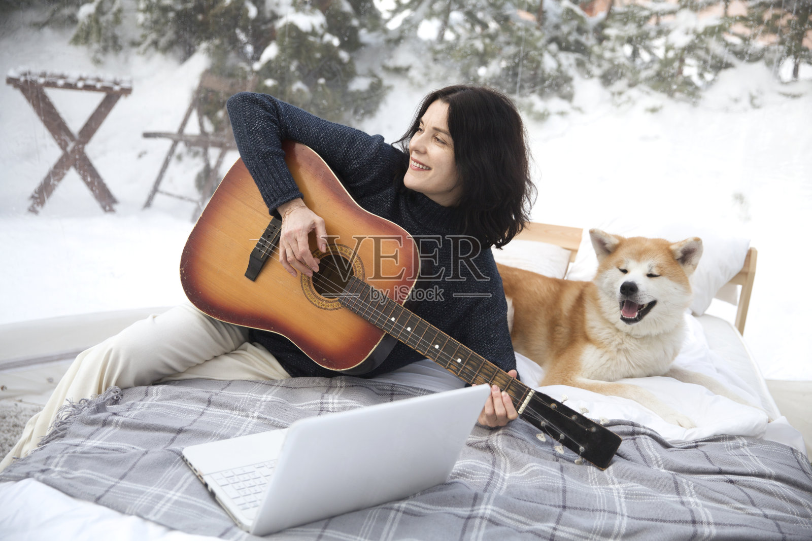 一名带着狗狗的中年妇女在寒假的Glamping房子里玩着吉他和笔记本电脑。照片摄影图片