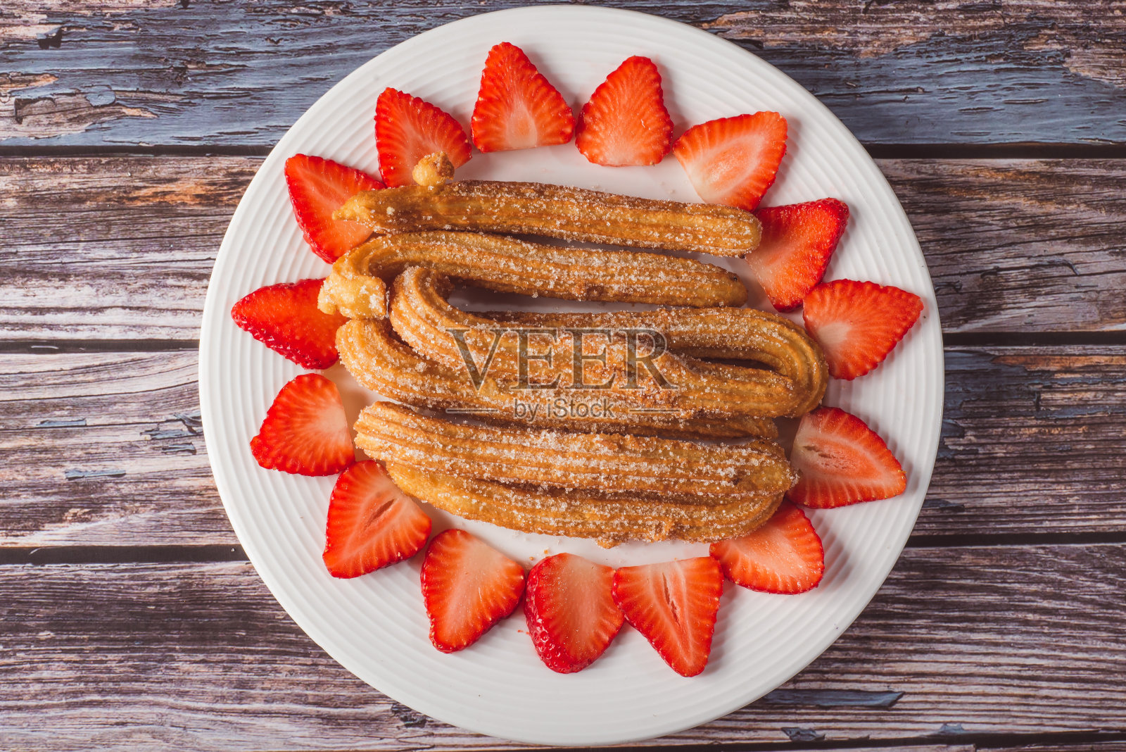 木桌上的白色盘子里放着油条和草莓片。照片摄影图片