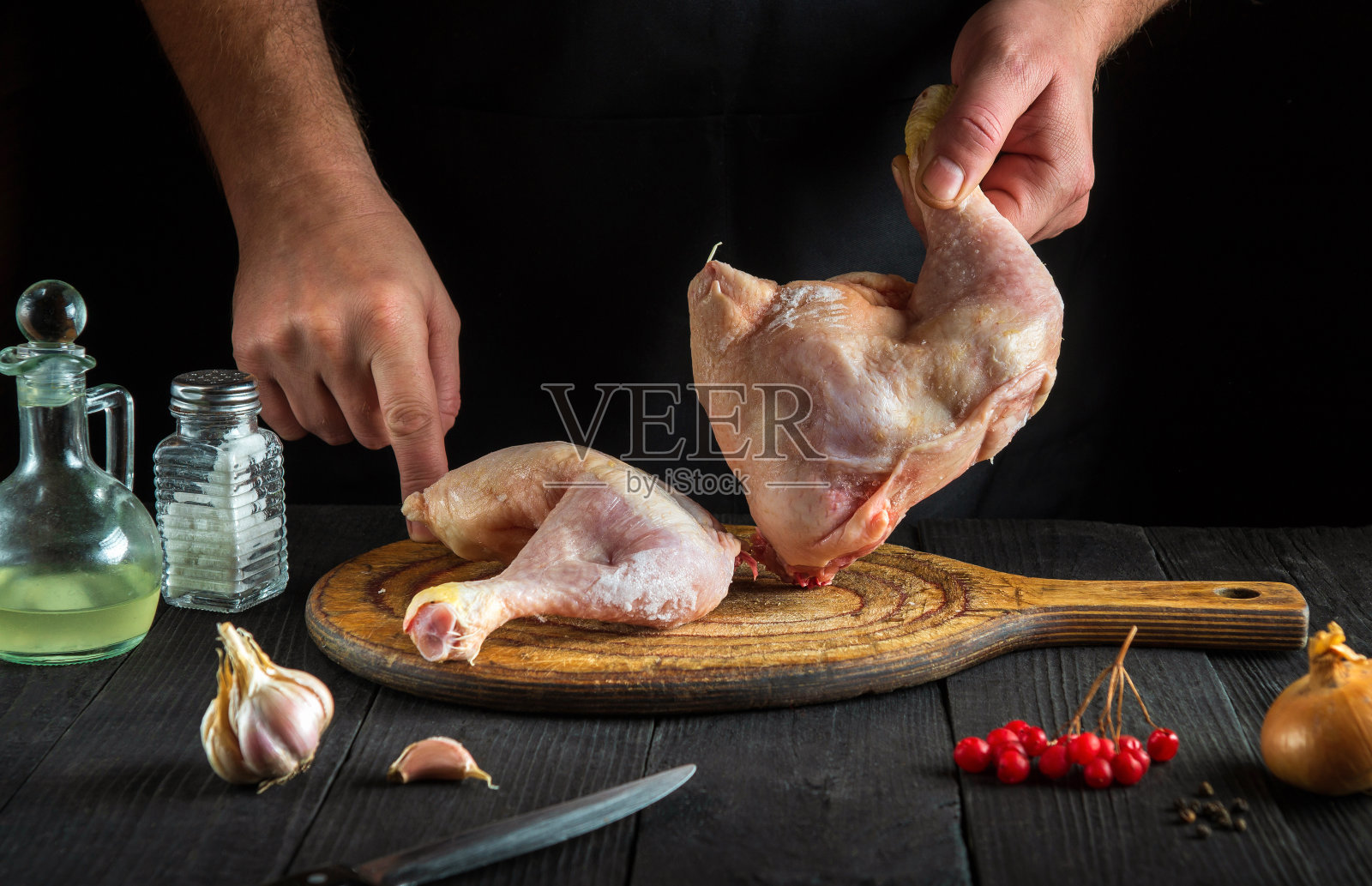 厨师在餐厅厨房里准备生鸡腿。厨师手里拿着鸡腿照片摄影图片