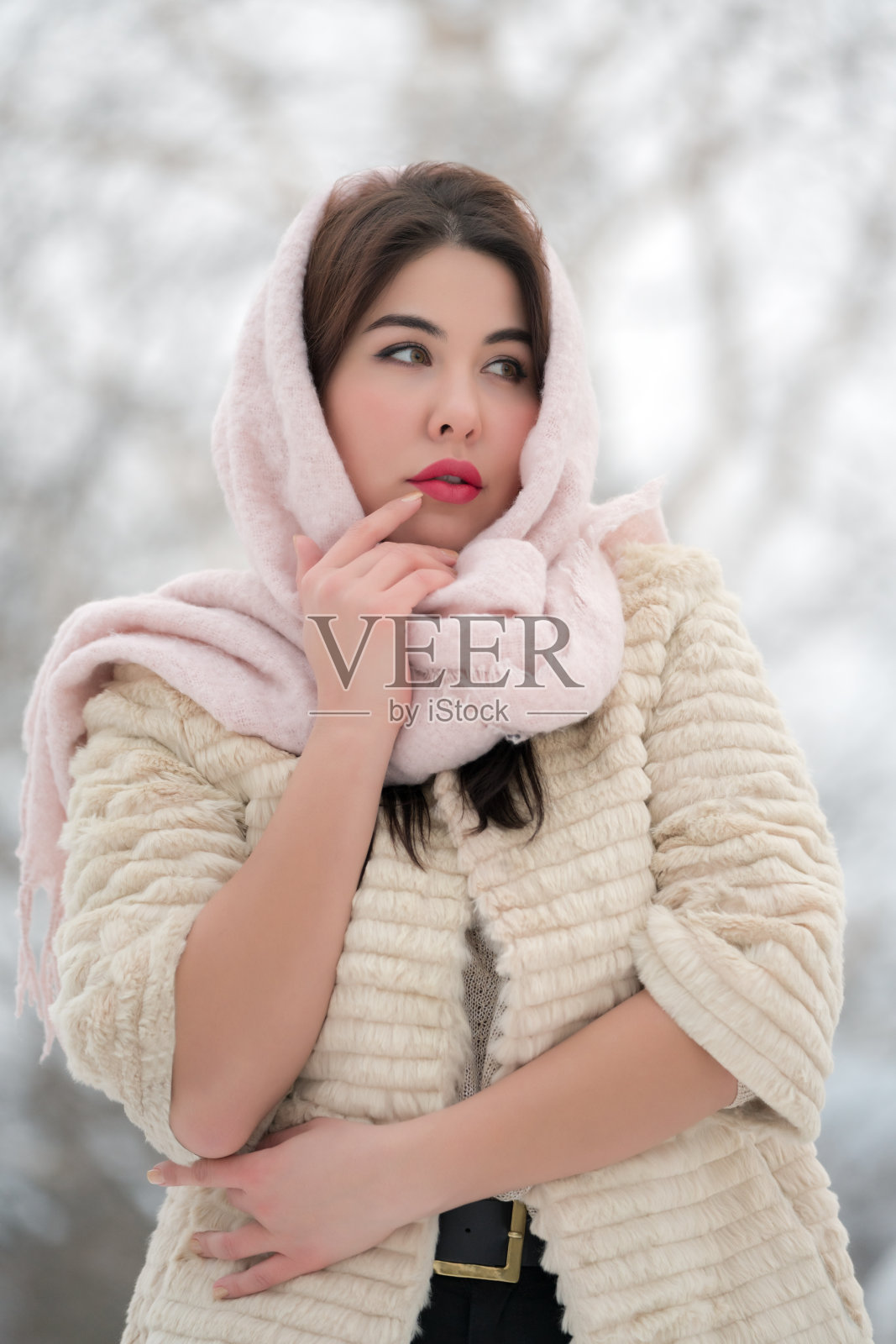 时尚的褐发年轻成人模特在白色毛皮大衣和浅粉色围巾在头上看向别处照片摄影图片