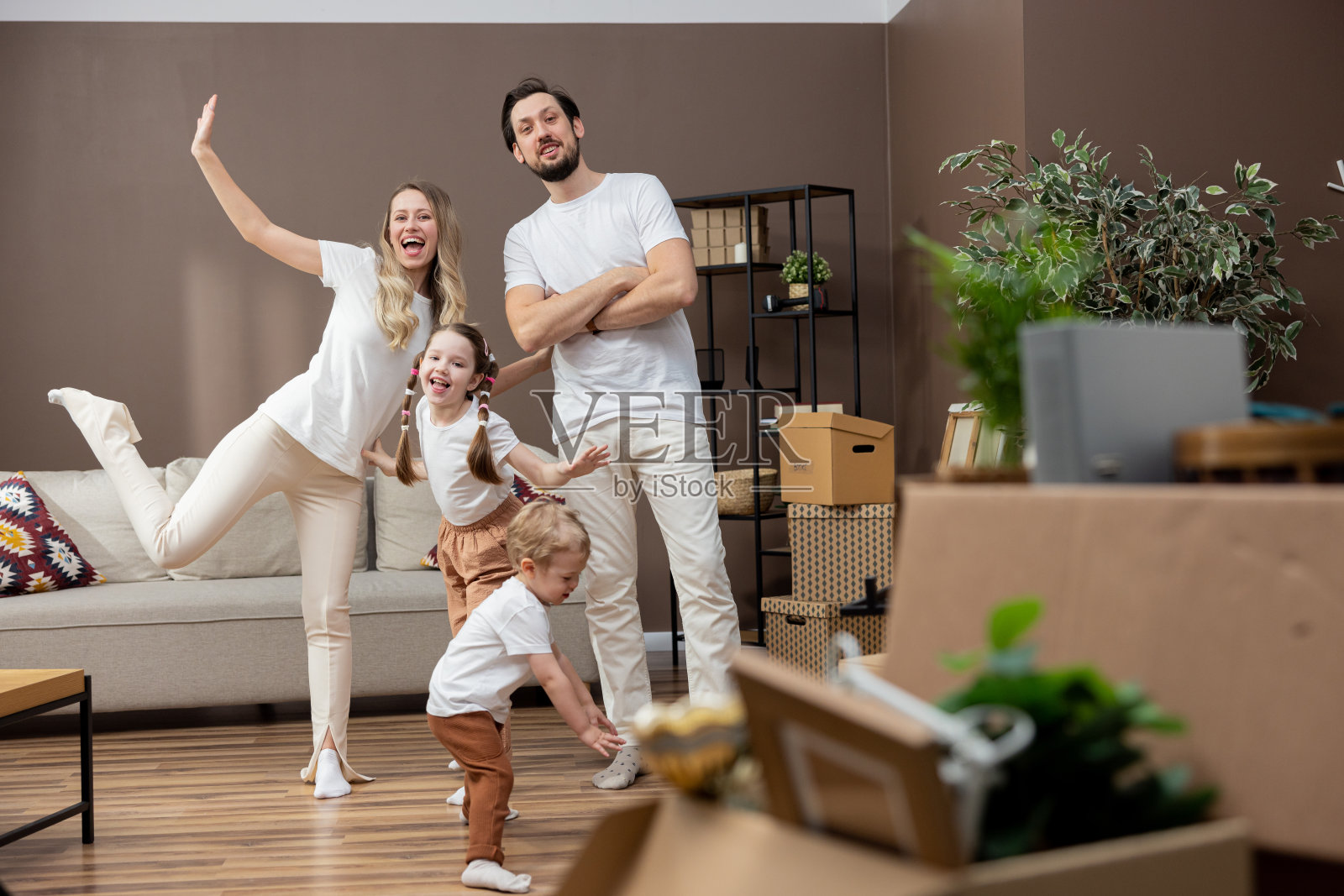 幸福的家庭，两个孩子在他们的新房子里玩耍。年轻的父母带着儿子和女儿在新房子里，到处都是纸板箱。他们微笑着，享受着搬家的乐趣照片摄影图片