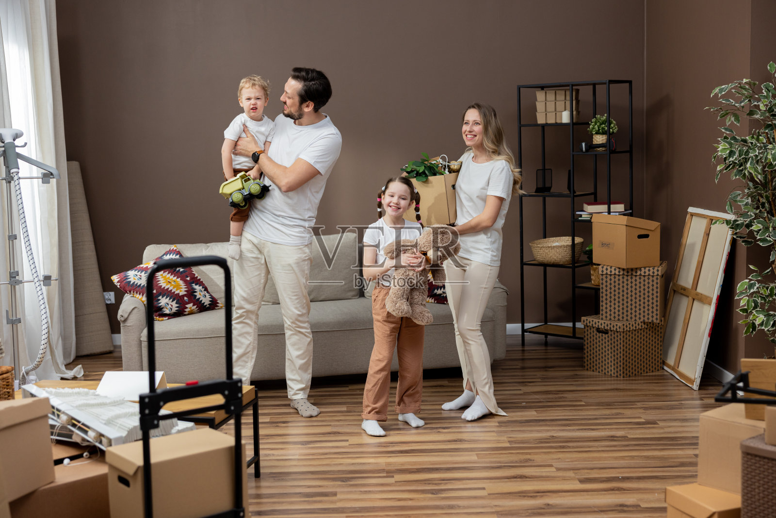幸福的年轻白人家庭的肖像，孩子们站在新家，拿着纸板箱，微笑着看着相机。房地产，购买房产，搬家或公寓概念照片摄影图片