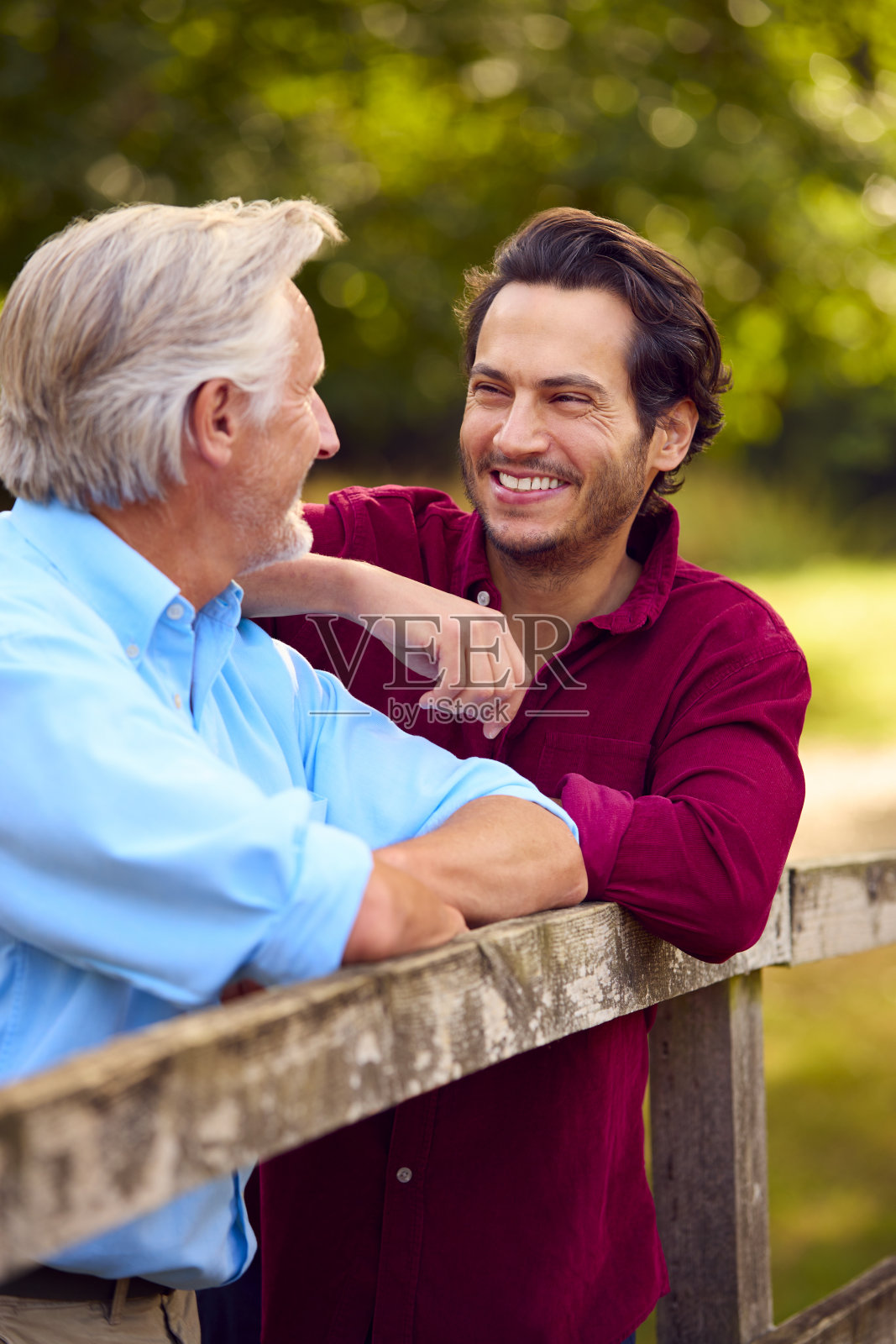 年长的父亲和混血成年儿子在乡间小路上靠着栅栏行走照片摄影图片