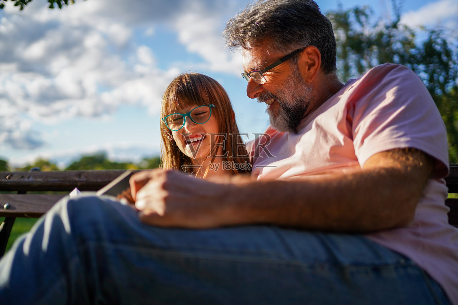 快乐的小女孩和爷爷在公园里读故事书。照片摄影图片