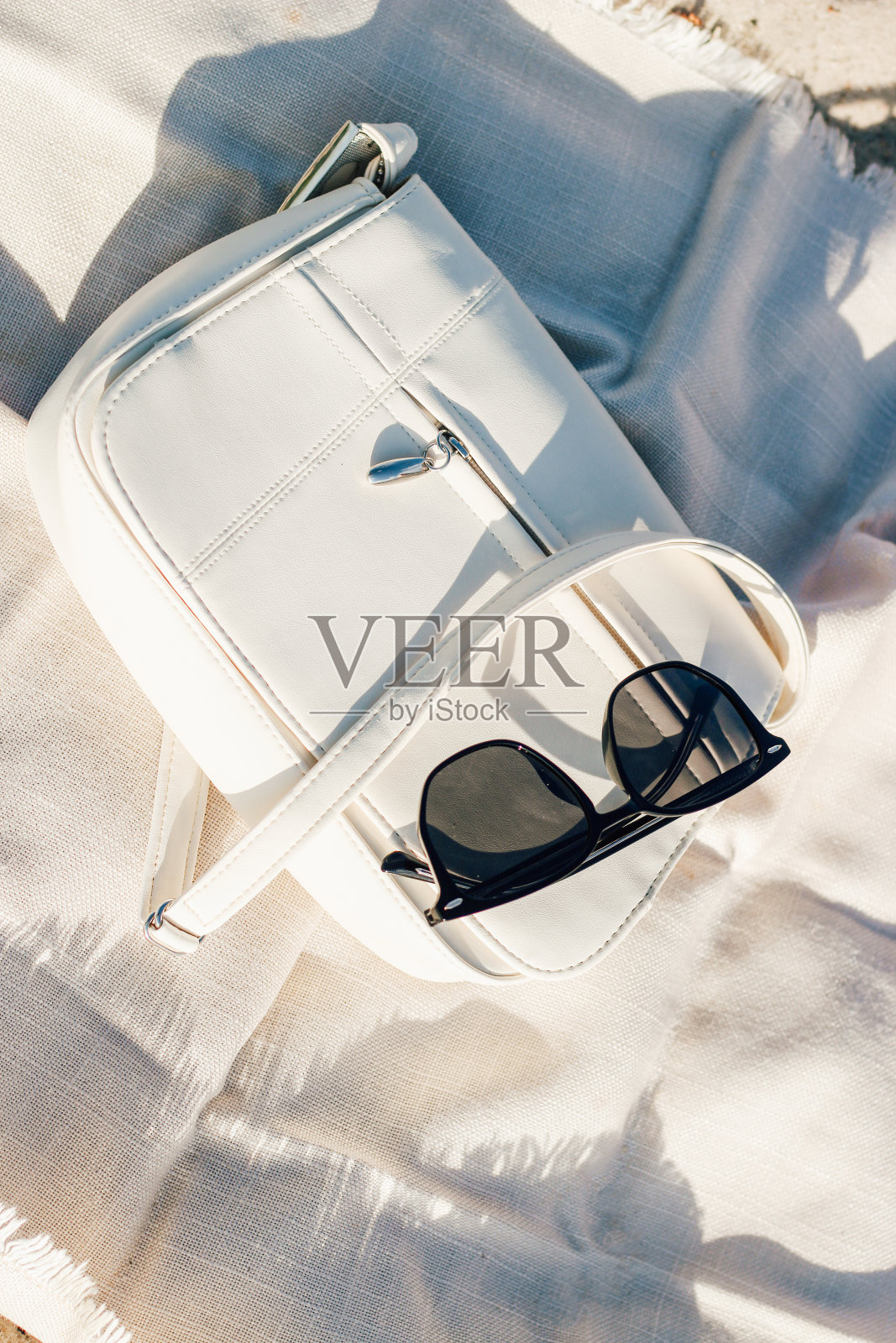 太阳眼镜和一个时髦的白色包在阳光的毯子上照片摄影图片
