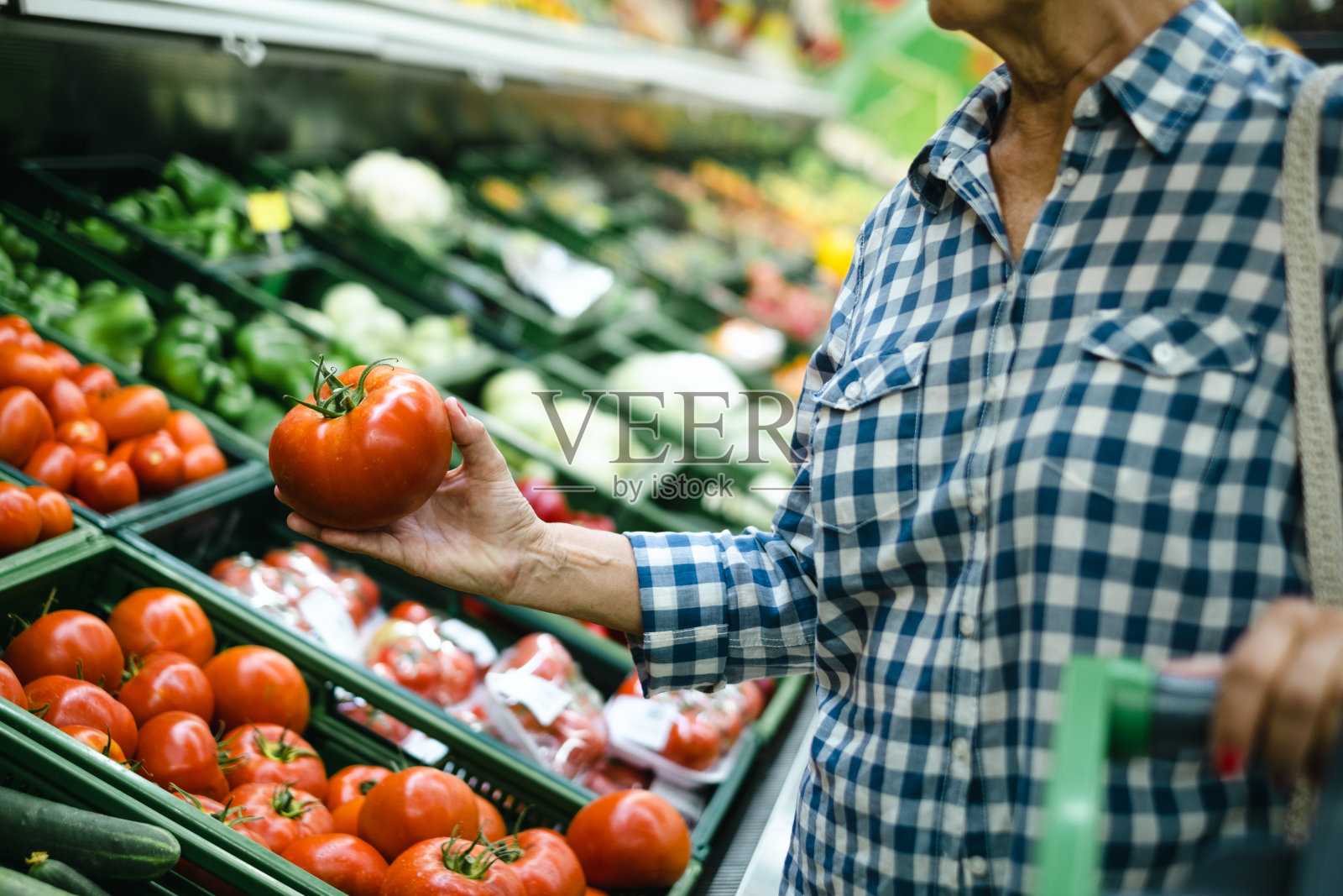 一位老妇人在超市挑选生蔬菜，手里拿着一个红番茄照片摄影图片