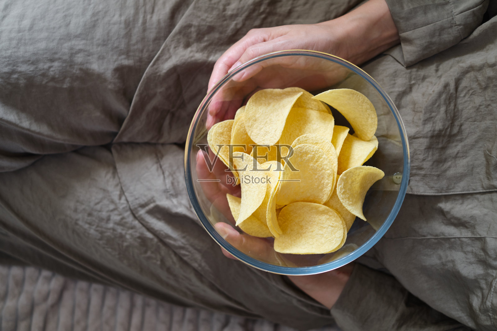 一个女人在沙发上吃着透明碗里的脆薯片。快餐。卡路里和饮食照片摄影图片