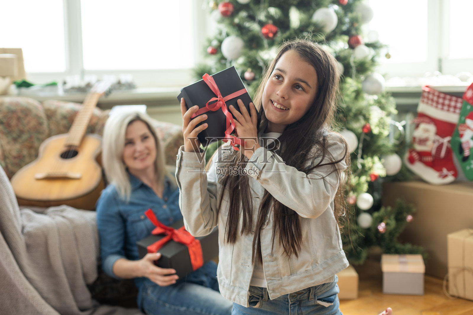 圣诞快乐，节日快乐。快乐的妈妈和她可爱的女儿交换礼物。妈妈和小孩在室内的树旁玩耍。爱的家庭，房间里有礼物照片摄影图片