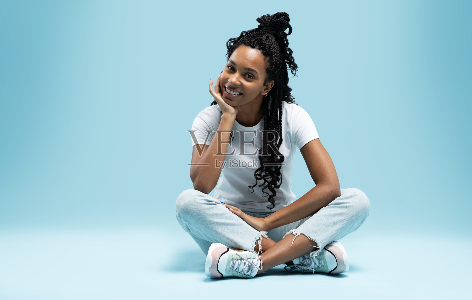 微笑年轻的非洲裔美国妇女休息，而坐在地板上双腿交叉孤立的蓝色背景照片摄影图片