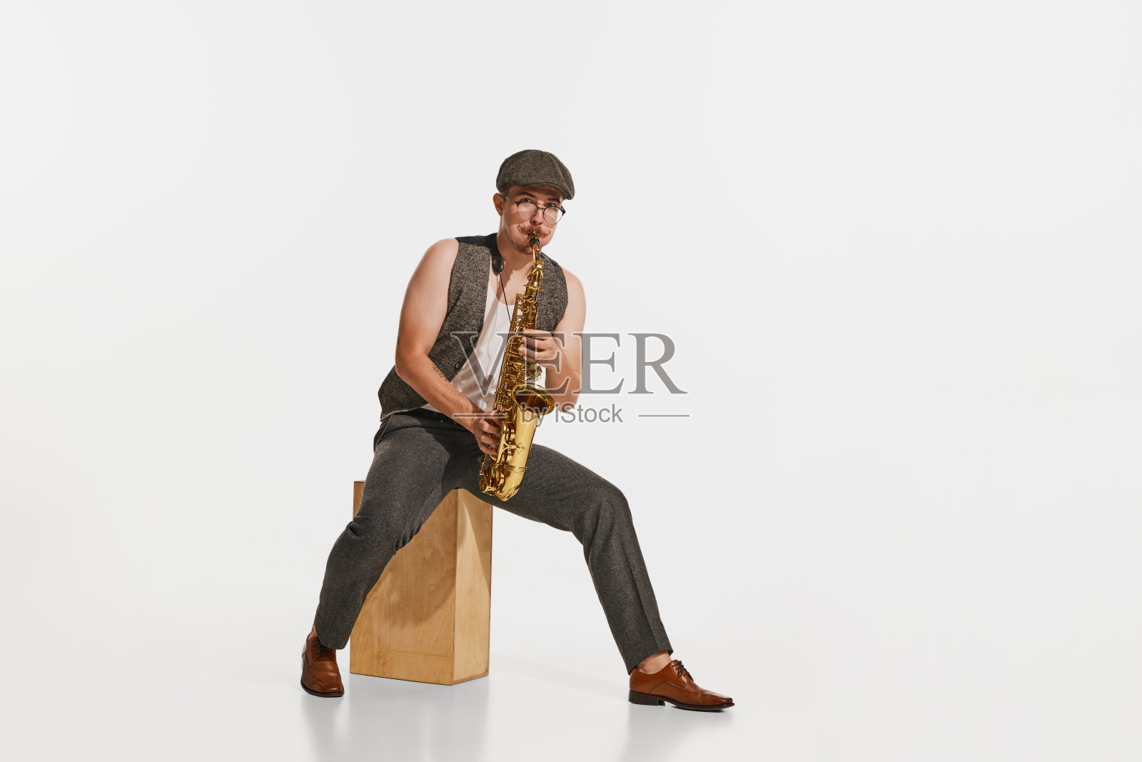 年轻的音乐家在复古风格的服装演奏萨克斯风孤立在白色的工作室背景。音乐、爱好、节日的概念。照片摄影图片