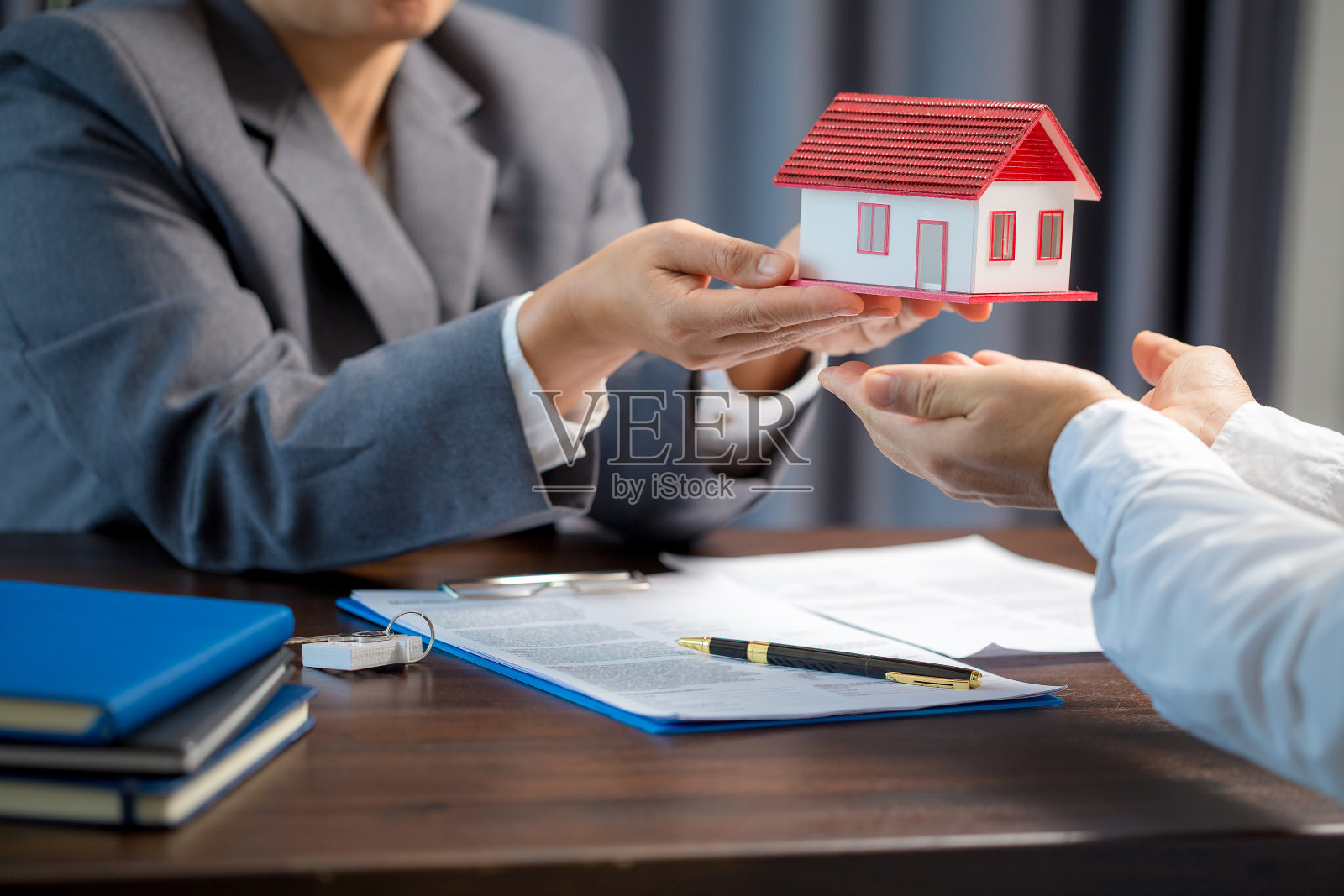 女性房屋销售人员在让客户签订购房合同之前，正在检查合同文件，表格上的房屋模型、房地产交易和保险财产概念是关键照片摄影图片