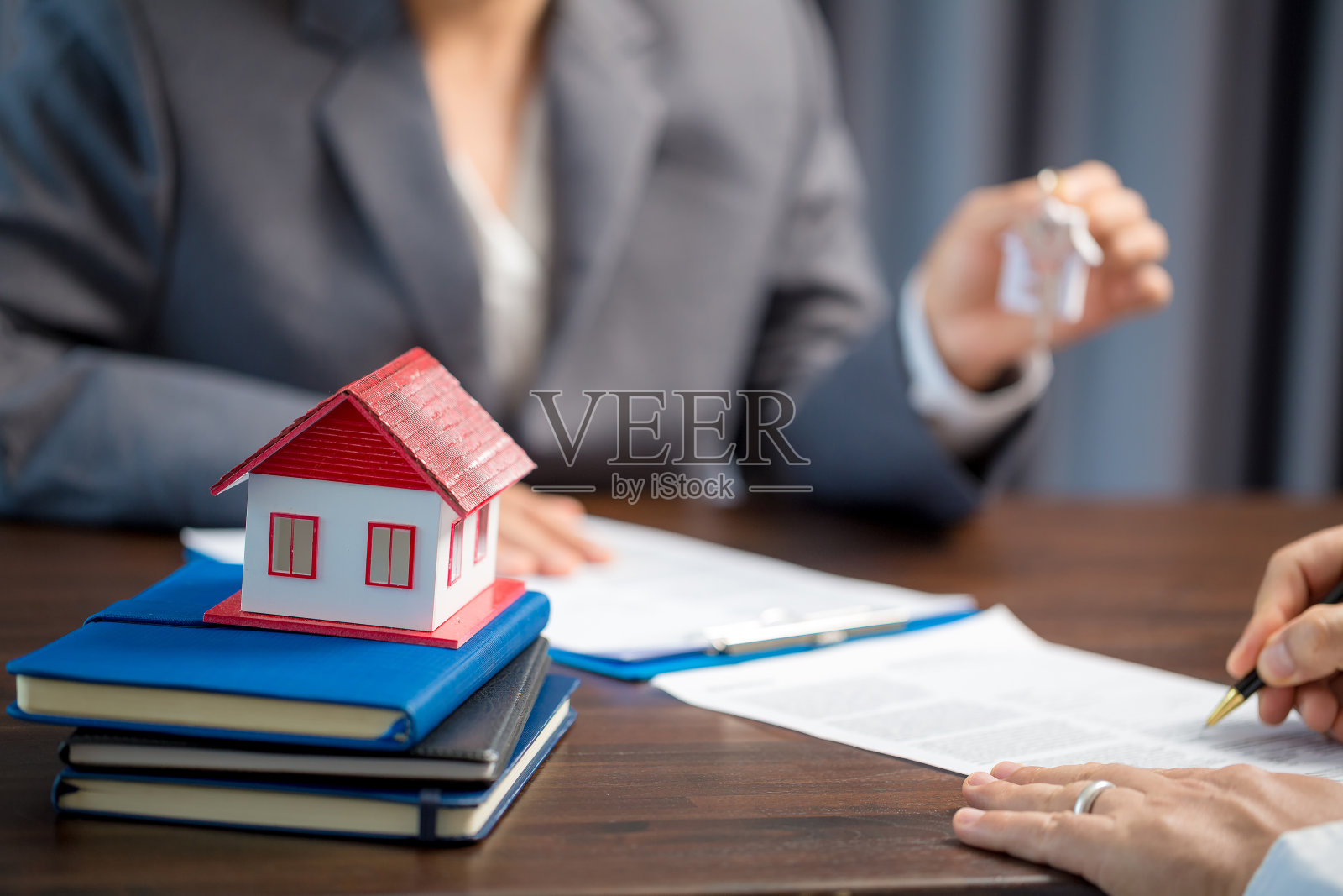 女性房屋销售人员在让客户签订购房合同之前，正在检查合同文件，表格上的房屋模型、房地产交易和保险财产概念是关键照片摄影图片