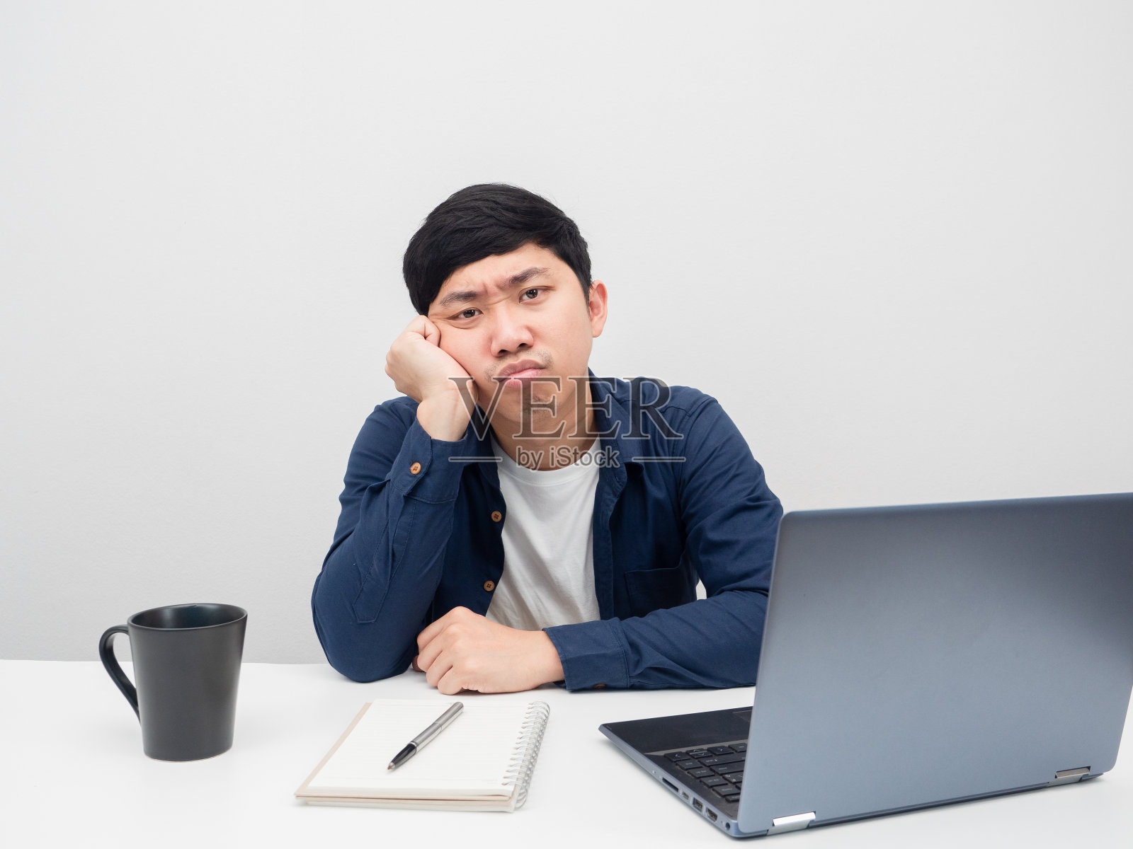 男人坐在桌子上用笔记本电脑工作感到无聊照片摄影图片