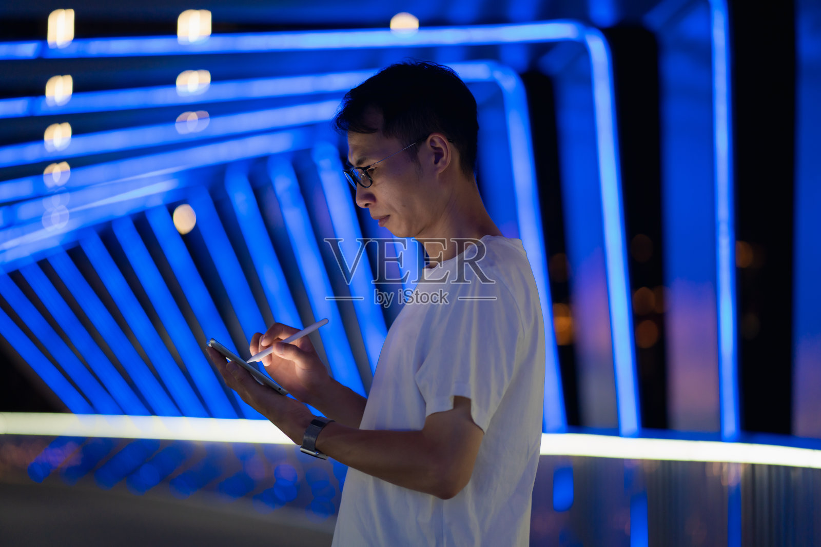 男子在蓝色霓虹灯背景上使用平板电脑照片摄影图片