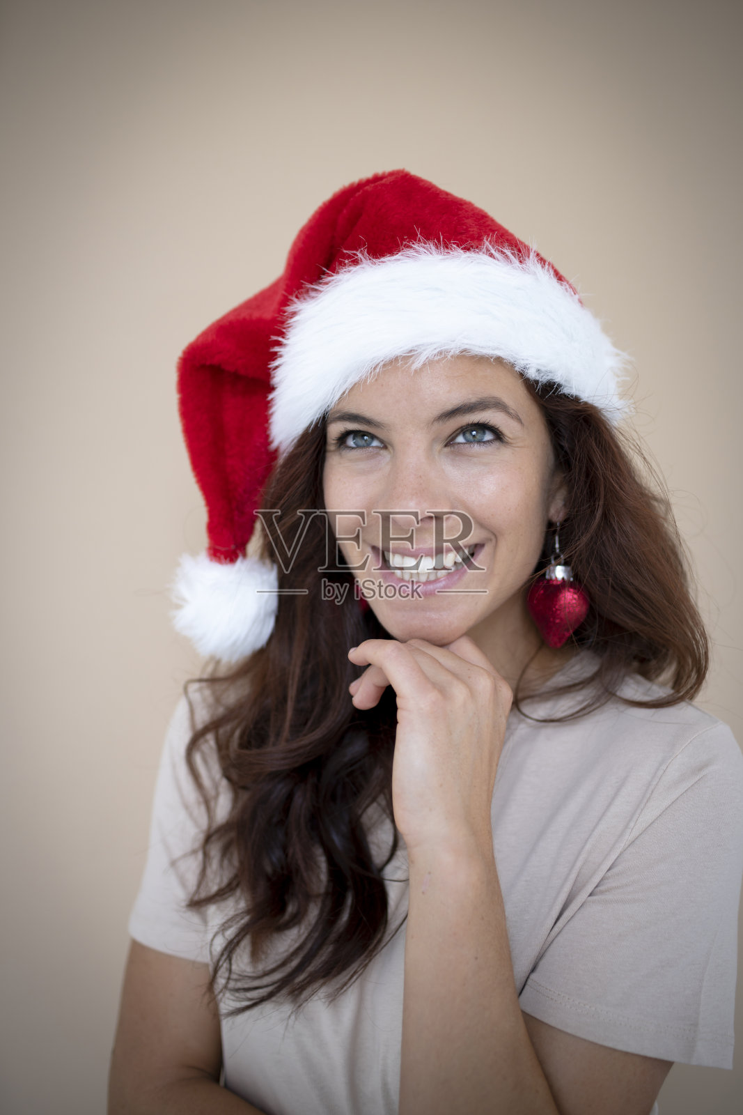 漂亮的年轻女子，深色头发，戴着圣诞帽和圣诞树球形状的心形耳环照片摄影图片