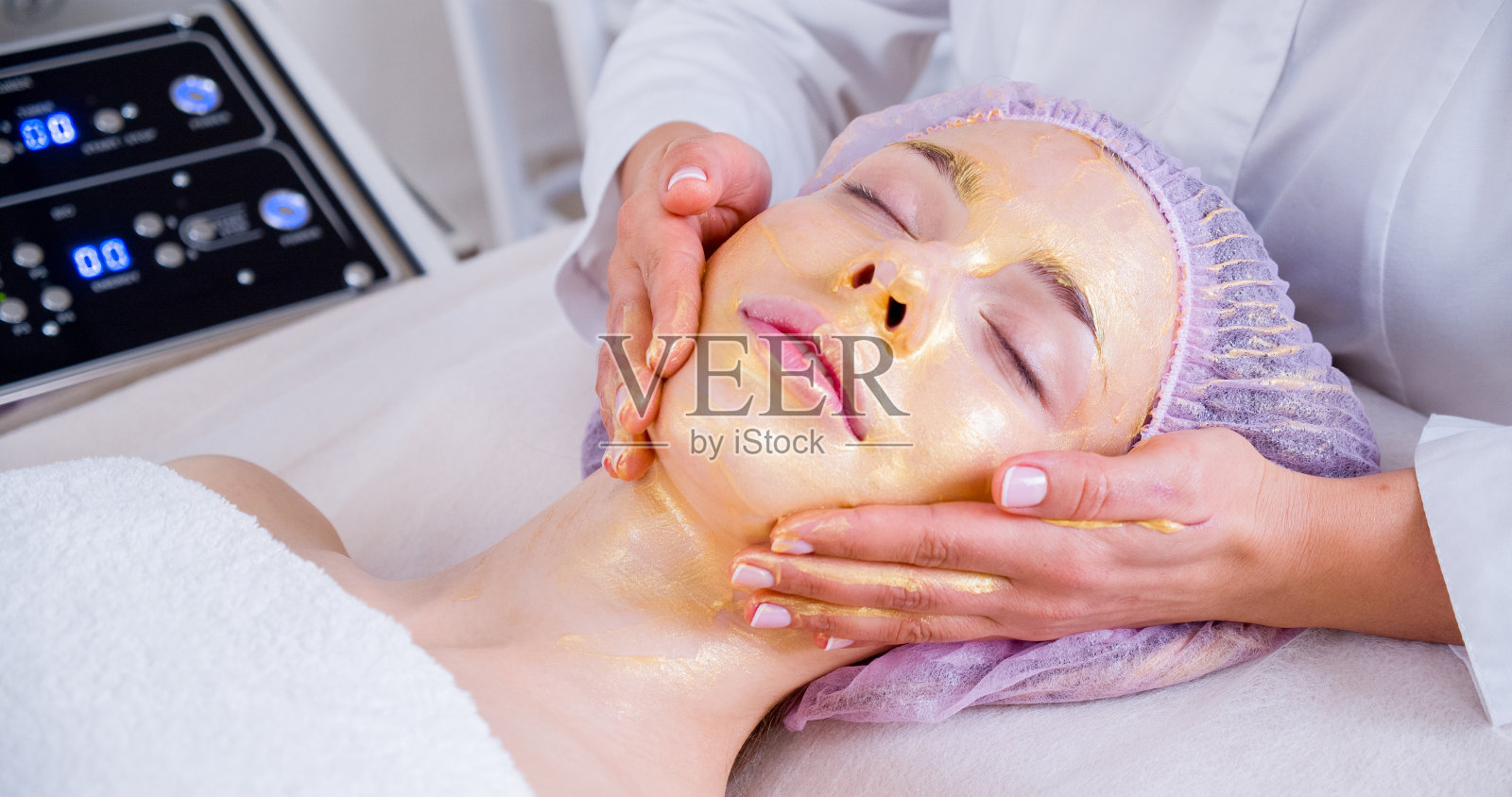 美容师给一位女士敷面膜。一名女子在水疗沙龙接受面部美容护理。美容师用保湿面膜在脸上按摩。照片摄影图片