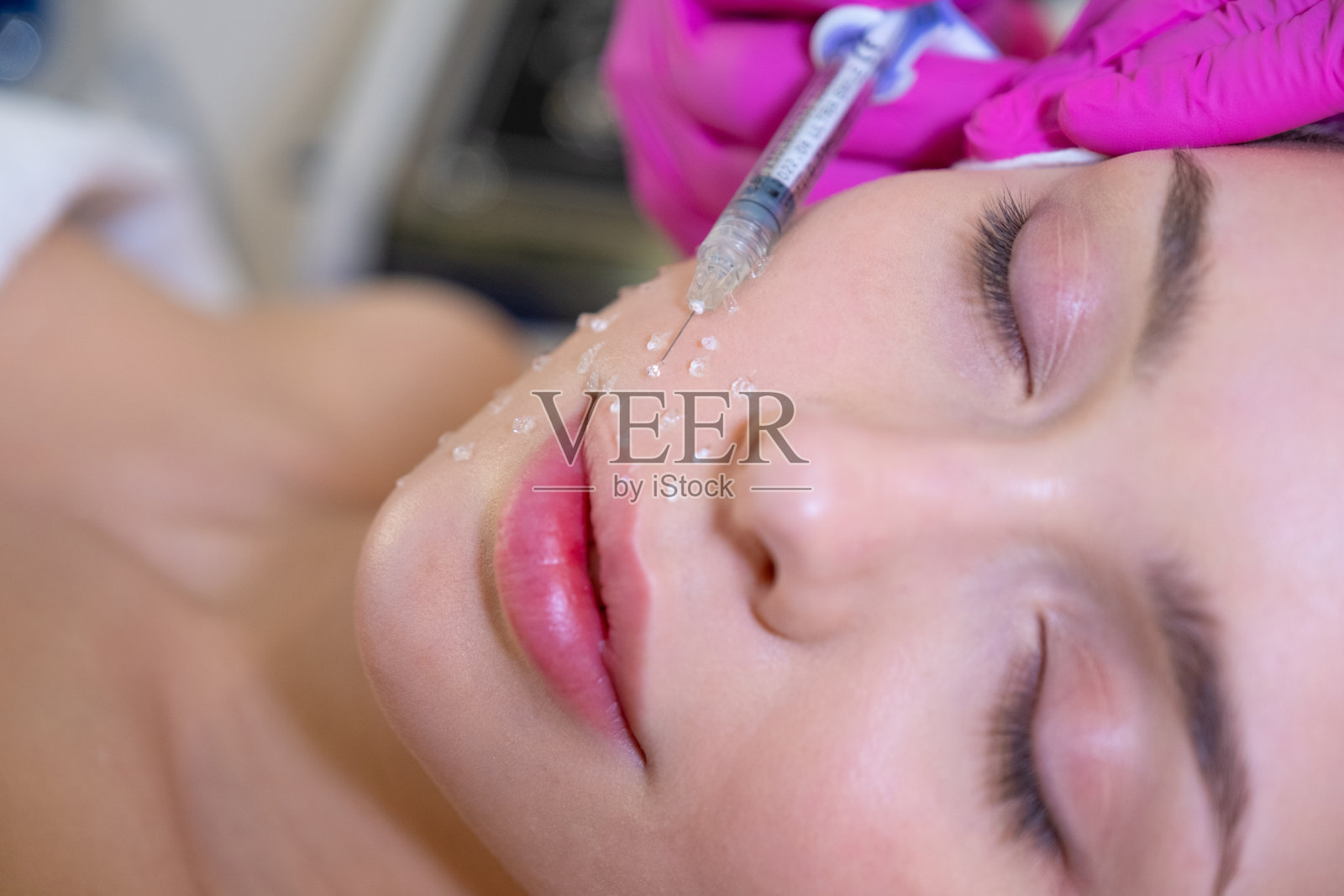 美容师用注射器把化妆品凝胶涂在妇女脸上。一名女子在水疗沙龙接受面部美容护理。美容师在脸上做皮肤护理程序。照片摄影图片