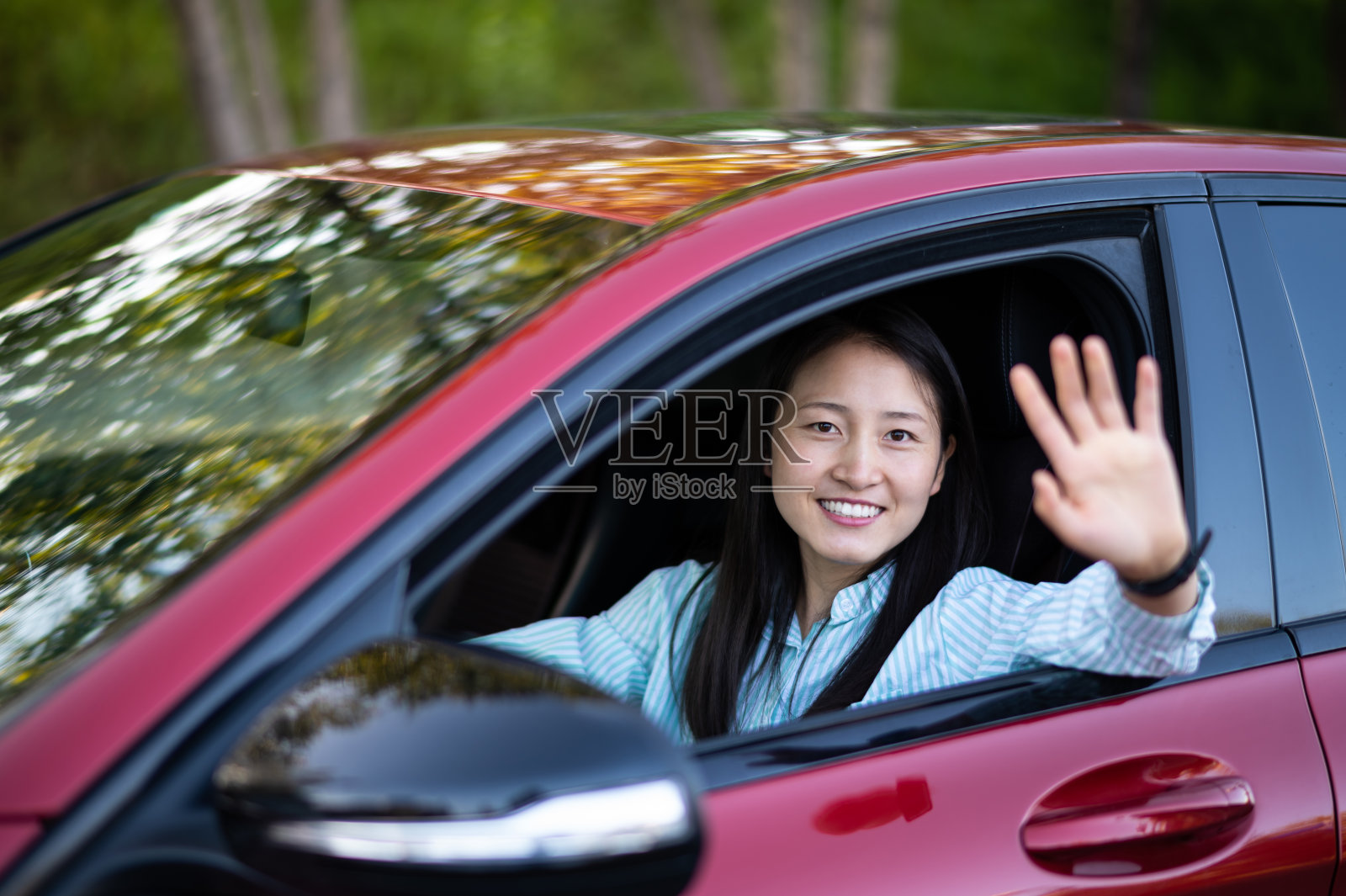 亚洲年轻女子坐在车里，把手伸出窗外，挥手照片摄影图片