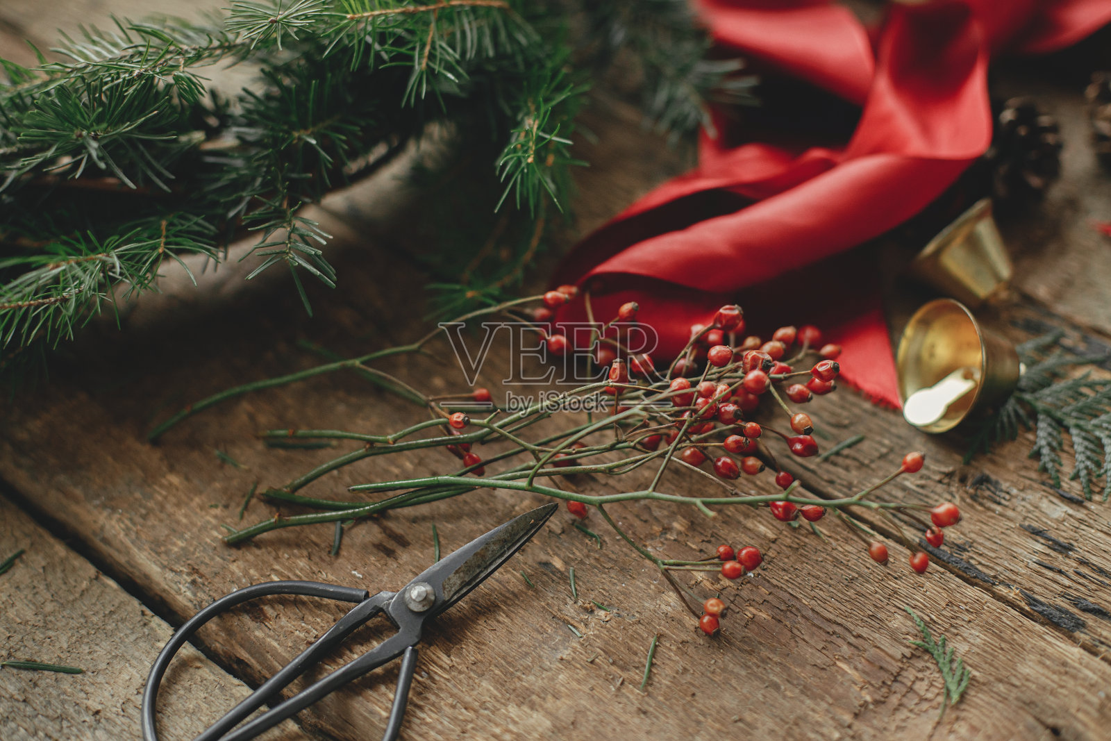 制作圣诞花环。冷杉树枝上圆圣诞花环，红丝带，浆果，剪刀在乡村木桌子。穆迪节日形象。假日作坊，冬季装饰照片摄影图片