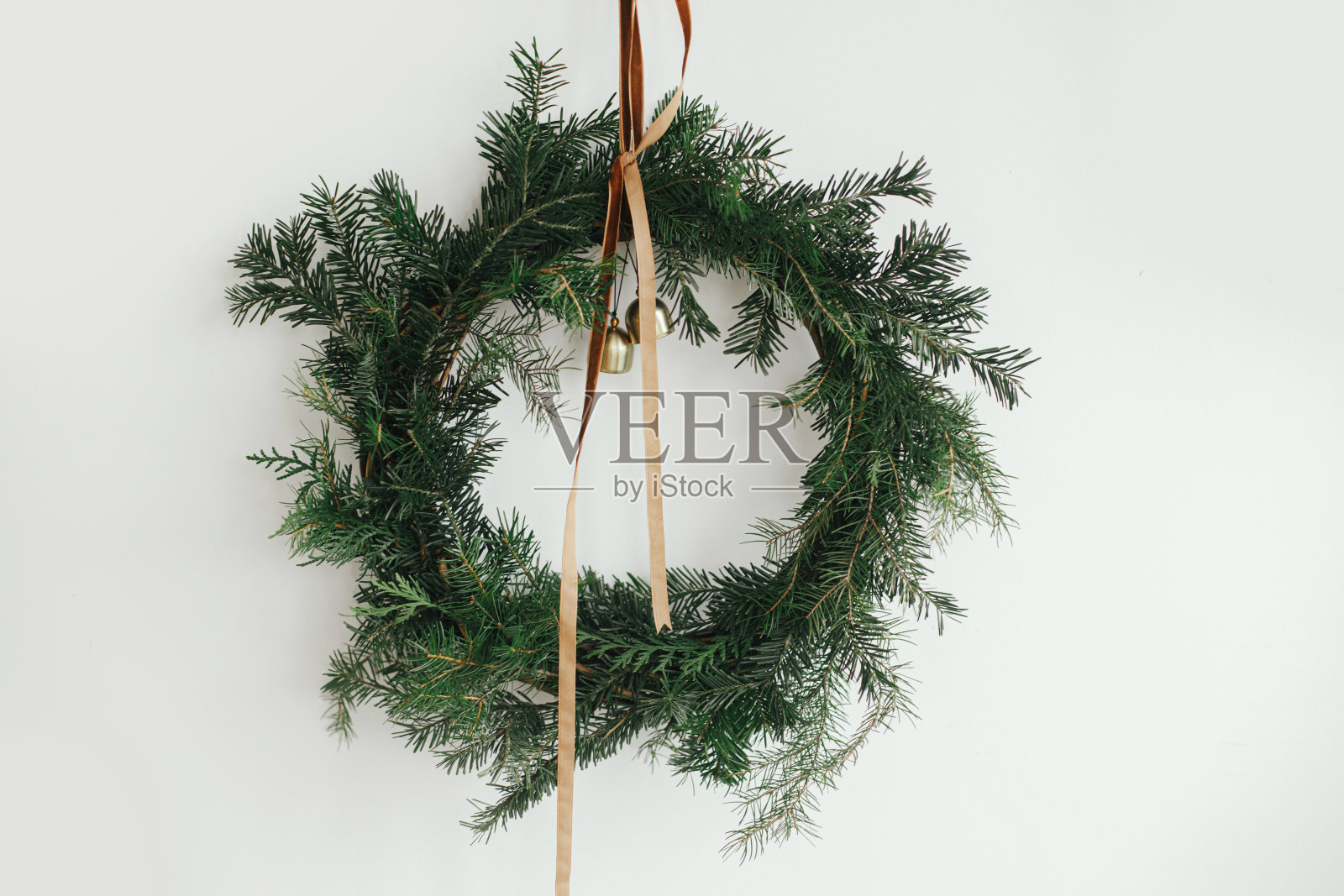 时尚的圣诞花环与丝绒丝带和金铃挂在白色的墙壁背景。圣诞乡村花环，忧郁形象。寒假装饰。圣诞快乐!照片摄影图片