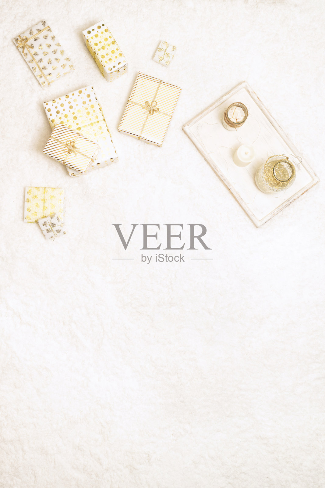 圣诞礼品盒包裹在白色的金色纸，为家庭躺在松软的雪白地毯托盘，andle和棉花糖。副本的空间。前视图。垂直比例照片摄影图片