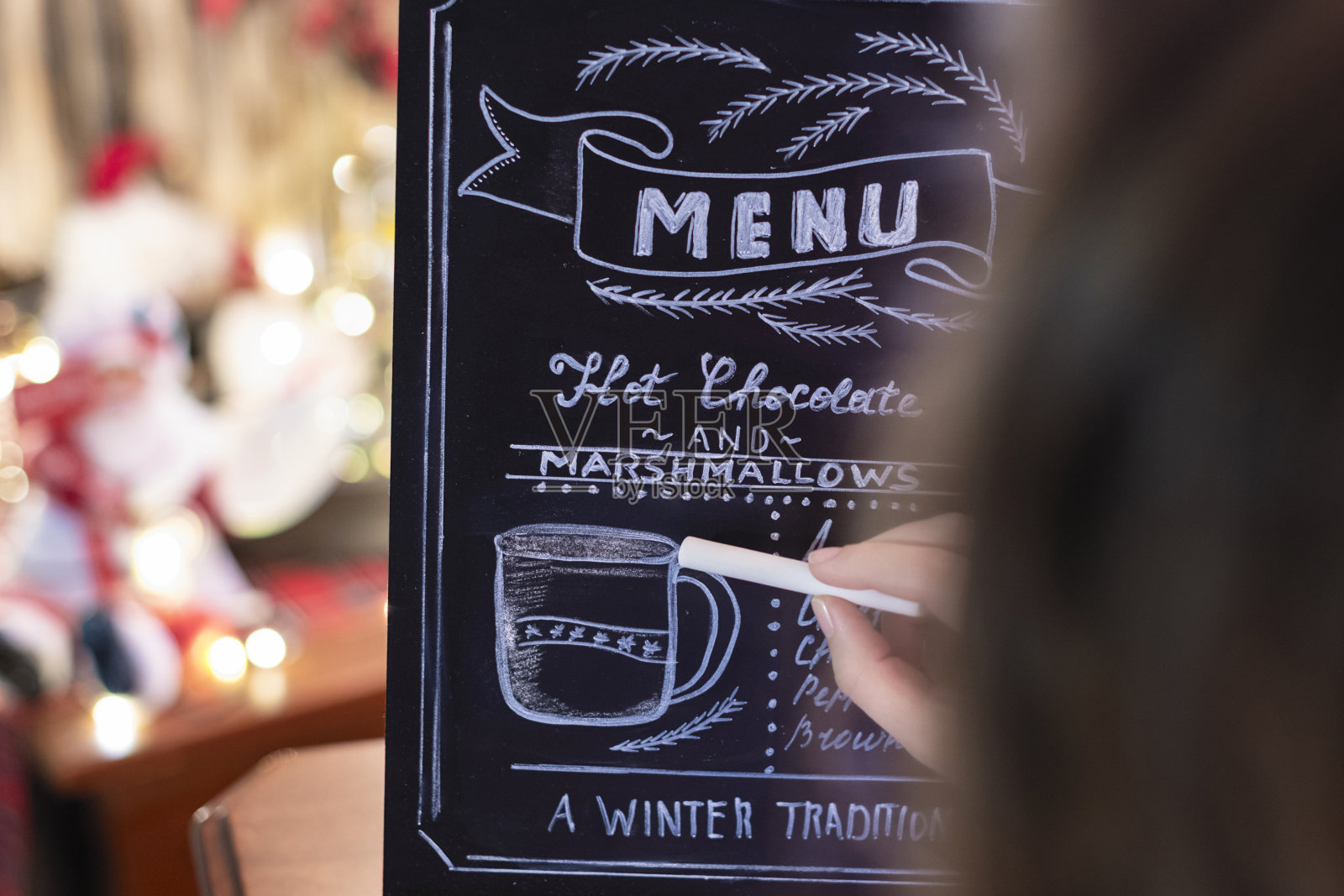 女士在小黑板上画圣诞巧克力棒菜单。照片摄影图片