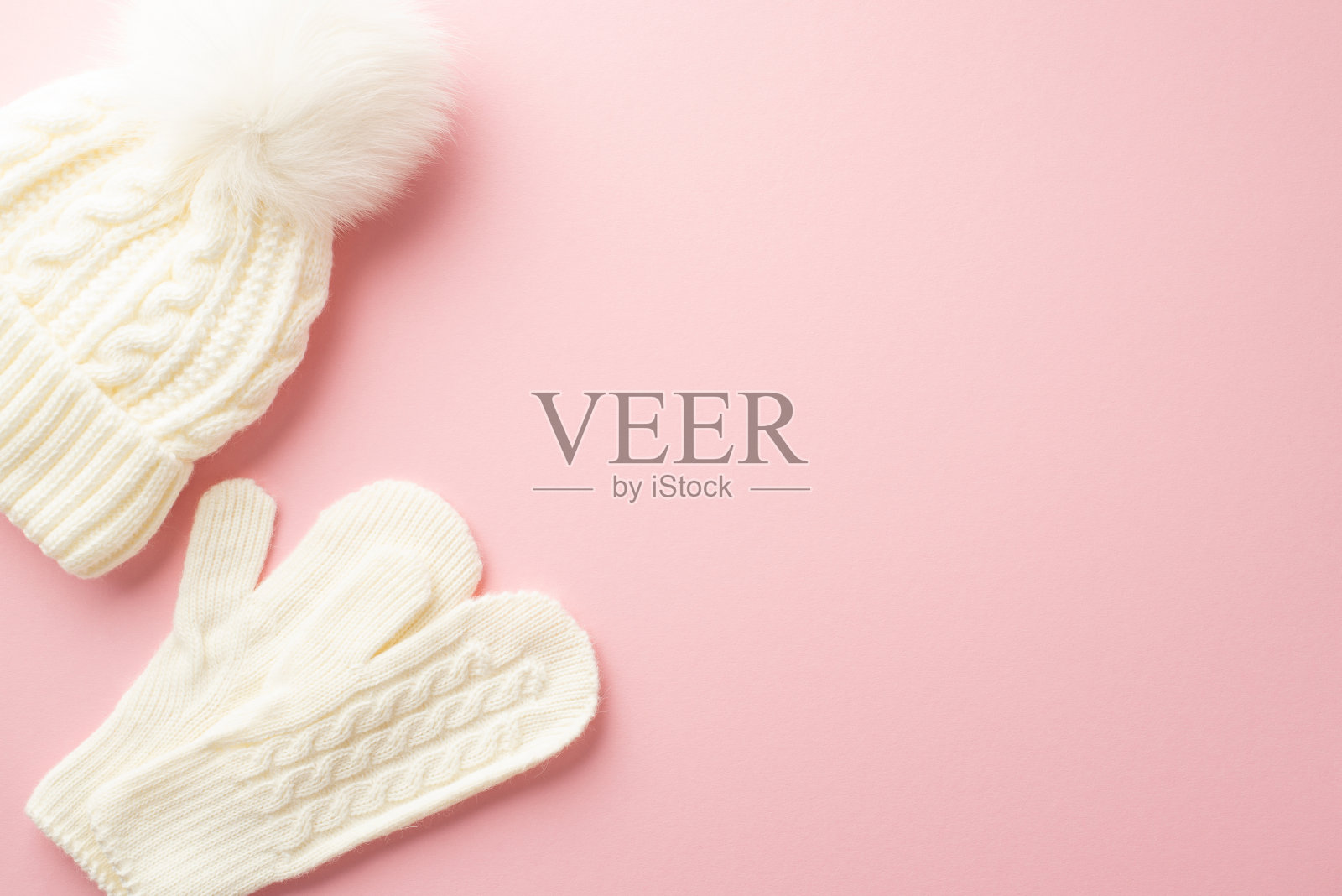 冬季的概念。顶视图照片的白色泡泡帽和针织手套在孤立的淡粉色背景与copyspace照片摄影图片