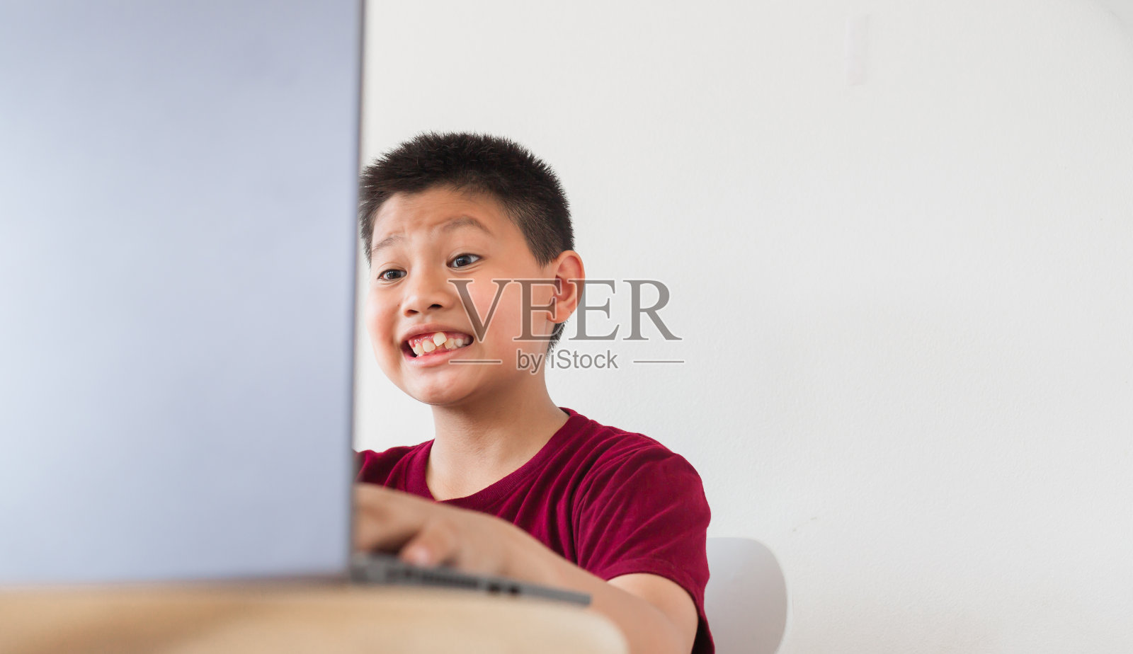 亚洲可爱小男孩与朋友在线聊天，对着笔记本电脑做鬼脸，看起来既震惊又兴奋照片摄影图片