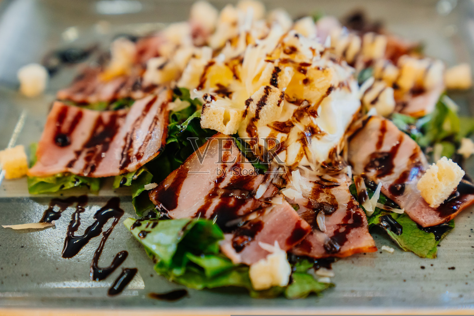 热沙拉配荷包蛋、培根和加酱的油炸面包丁，放在灰色盘子里。照片摄影图片