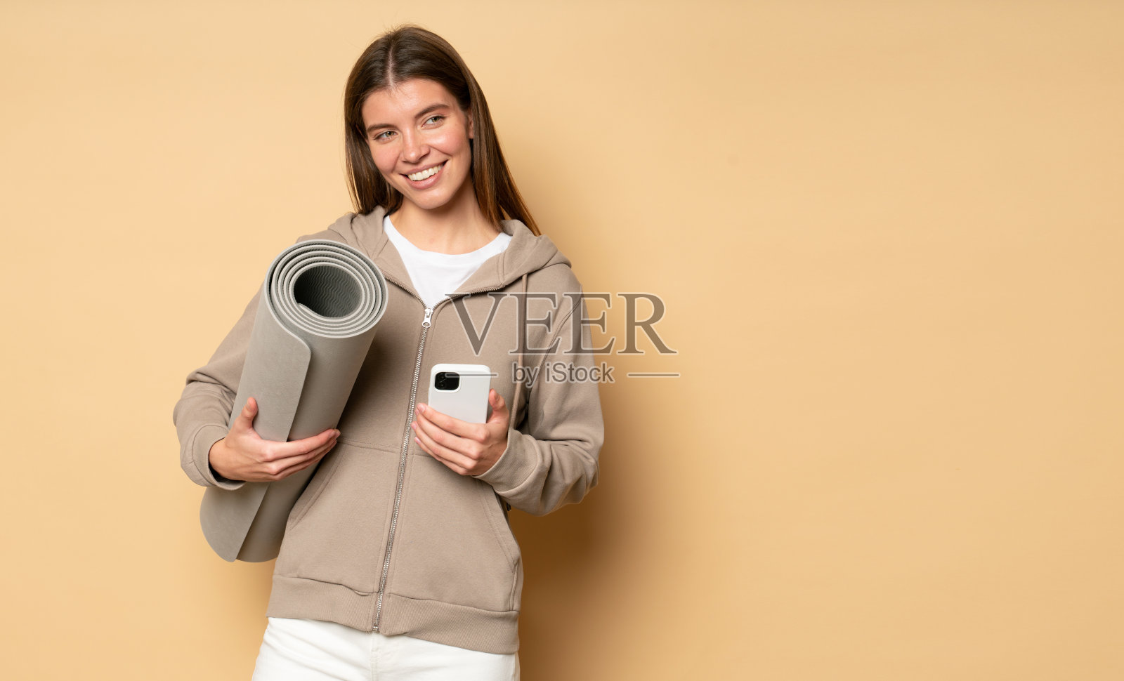 横幅健身妇女在卫衣与垫子和手机看着复制空间在棕色背景照片摄影图片