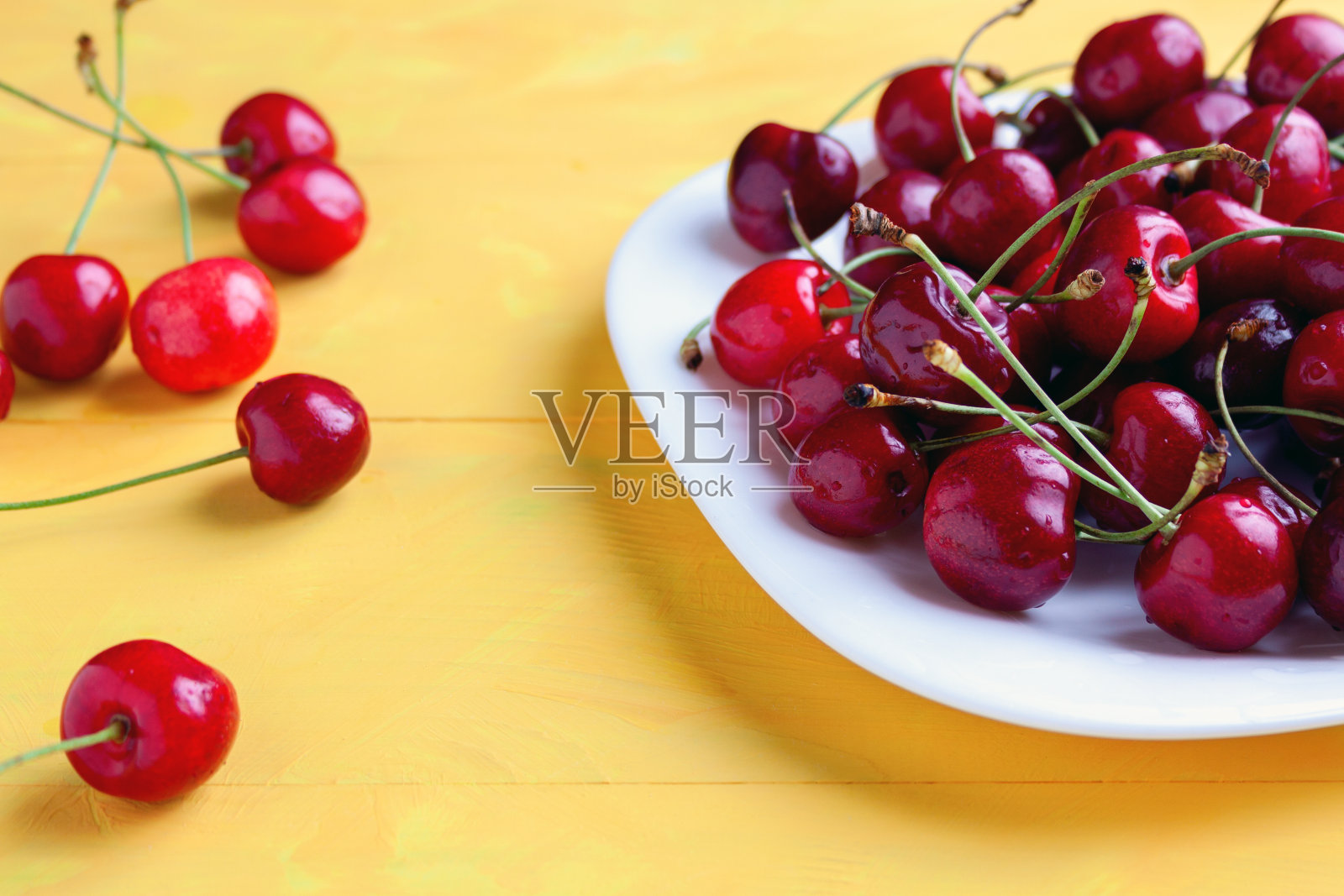 新鲜成熟的樱桃在碗与水滴，黄色的背景照片摄影图片