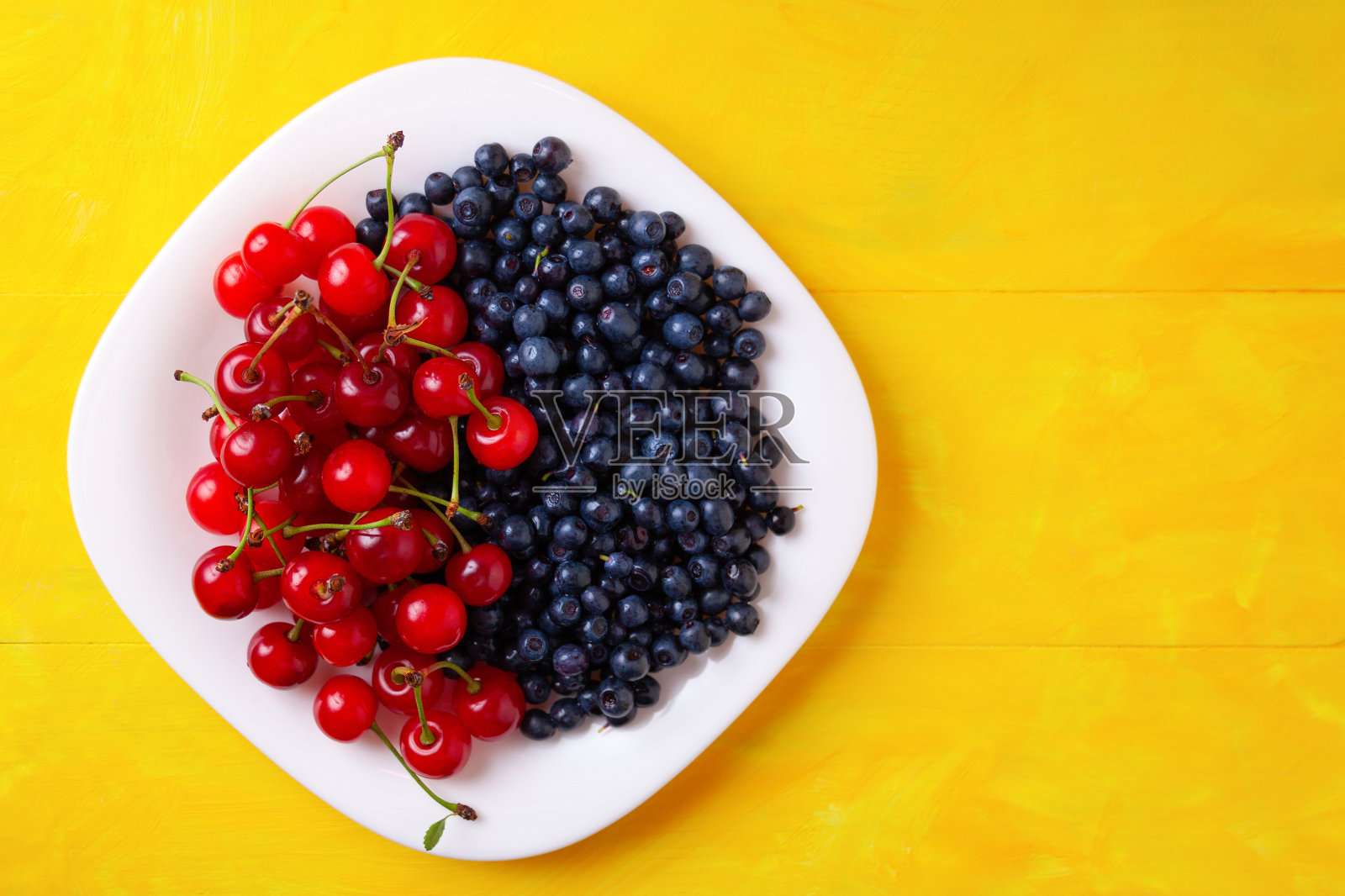 盘子里放着樱桃和蓝莓，夏天应季的浆果，放在黄色的木制背景上照片摄影图片