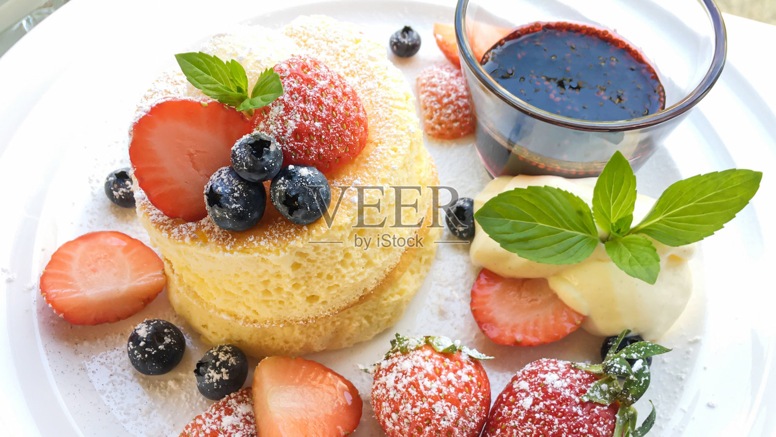 特写蓬松的日式soufflé煎饼，混合浆果甜点配浆果酱汁。照片摄影图片