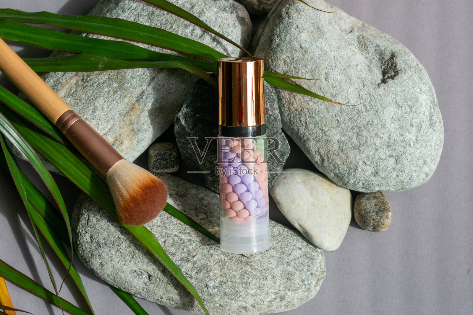 绿色树叶旁边的石头上放着一瓶化妆品，旁边放着一把刷子。化妆刷和化妆品照片摄影图片