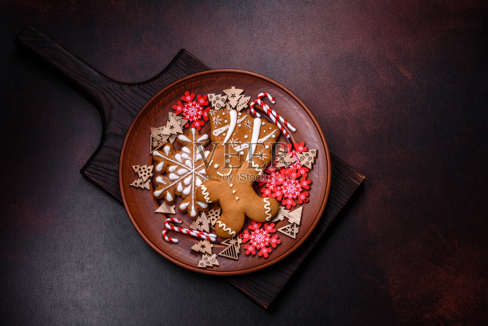 美丽的姜饼放在棕色陶瓷盘上，深色混凝土背景上有圣诞树装饰照片摄影图片