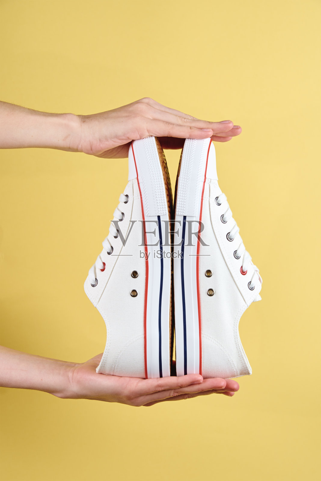 女人的手拿着黄色背景的休闲鞋照片摄影图片